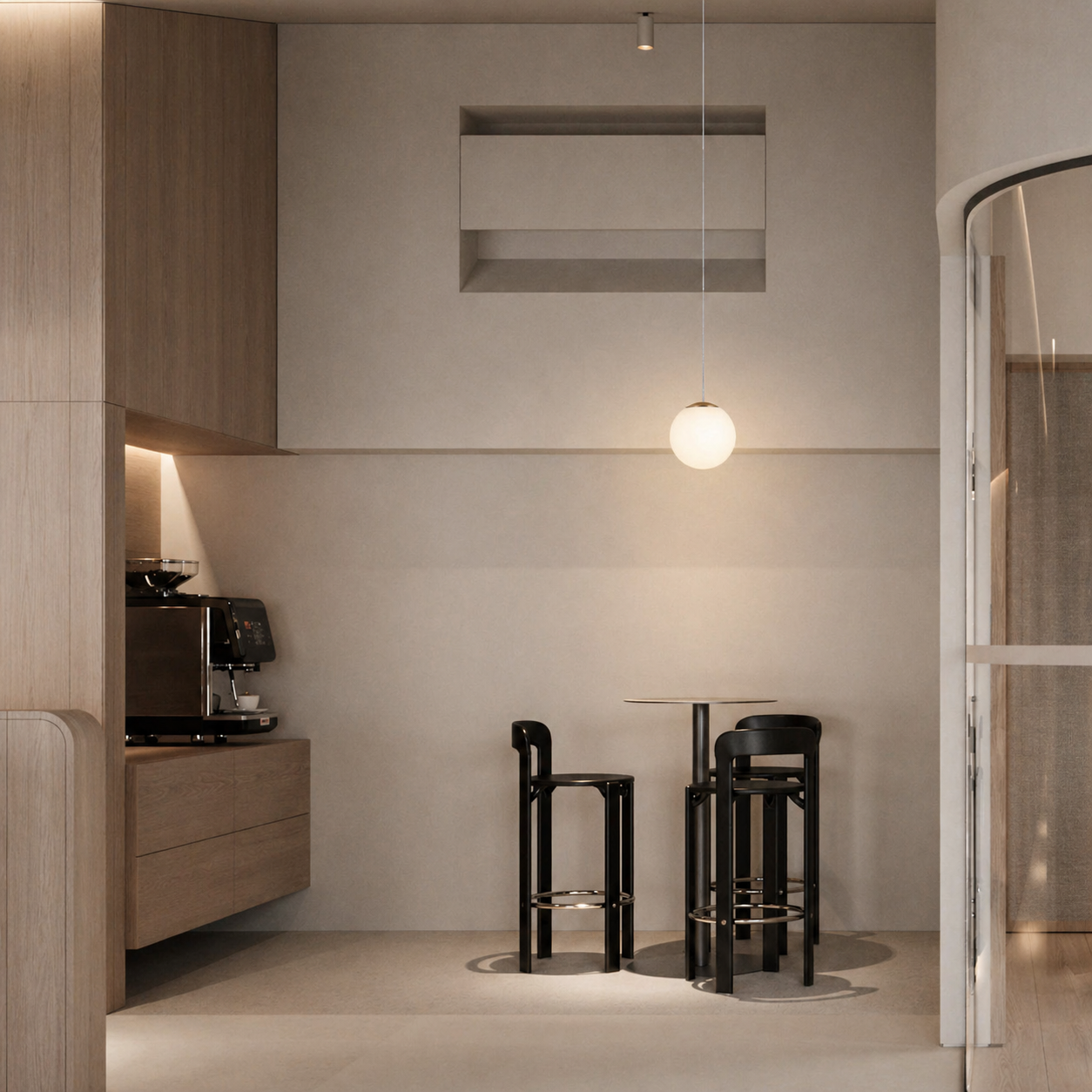 Minimalist kitchen dining area with wooden cabinetry, a coffee machine, a small round table, and three black bar stools. A spherical hanging light fixture provides soft illumination. Neutral-colored walls and modern decor create a clean, contemporary aesthetic.