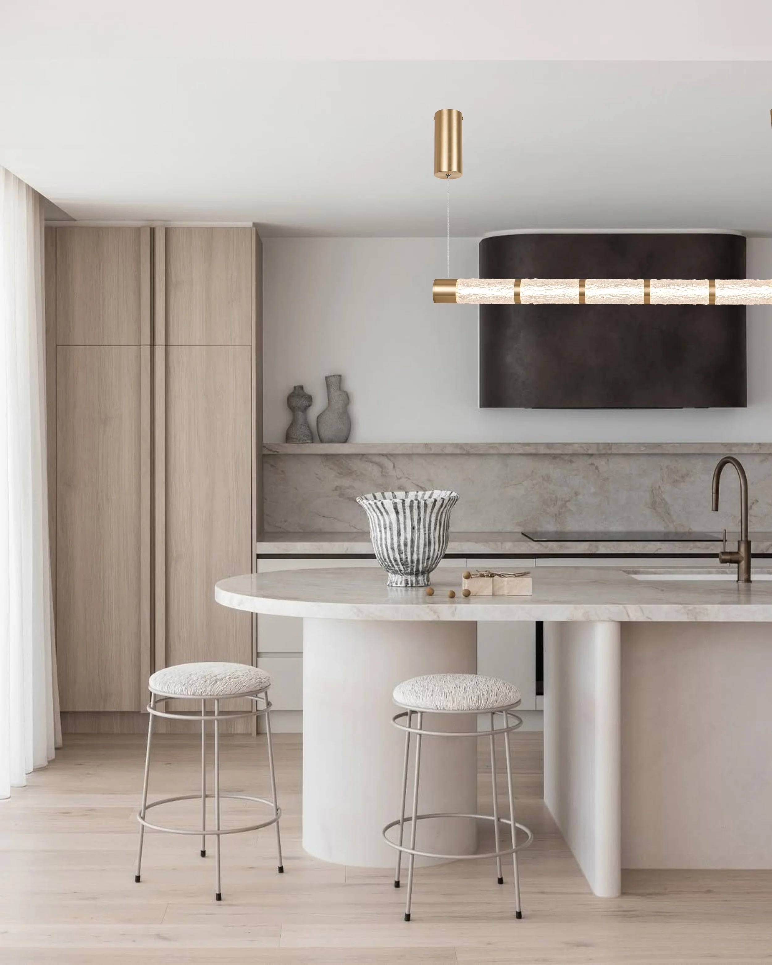Modern kitchen with a white marble countertop, two white cushioned barstools with metal frames, a striped black-and-white vase, wooden cabinetry, and minimalist decor.