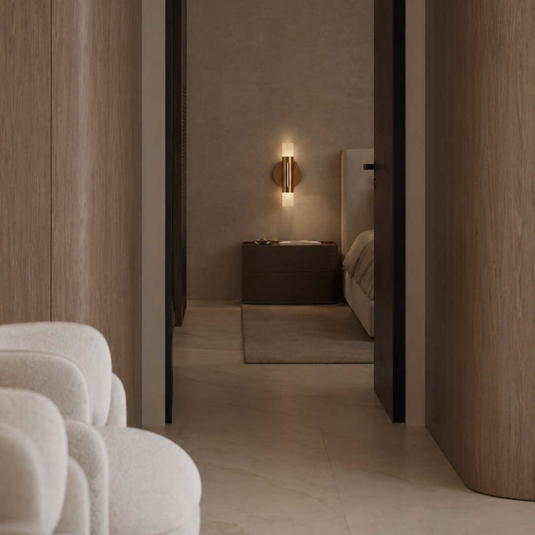 View into a modern hotel room from a hallway, showing a nightstand, wall lamp, bed, and textured walls.