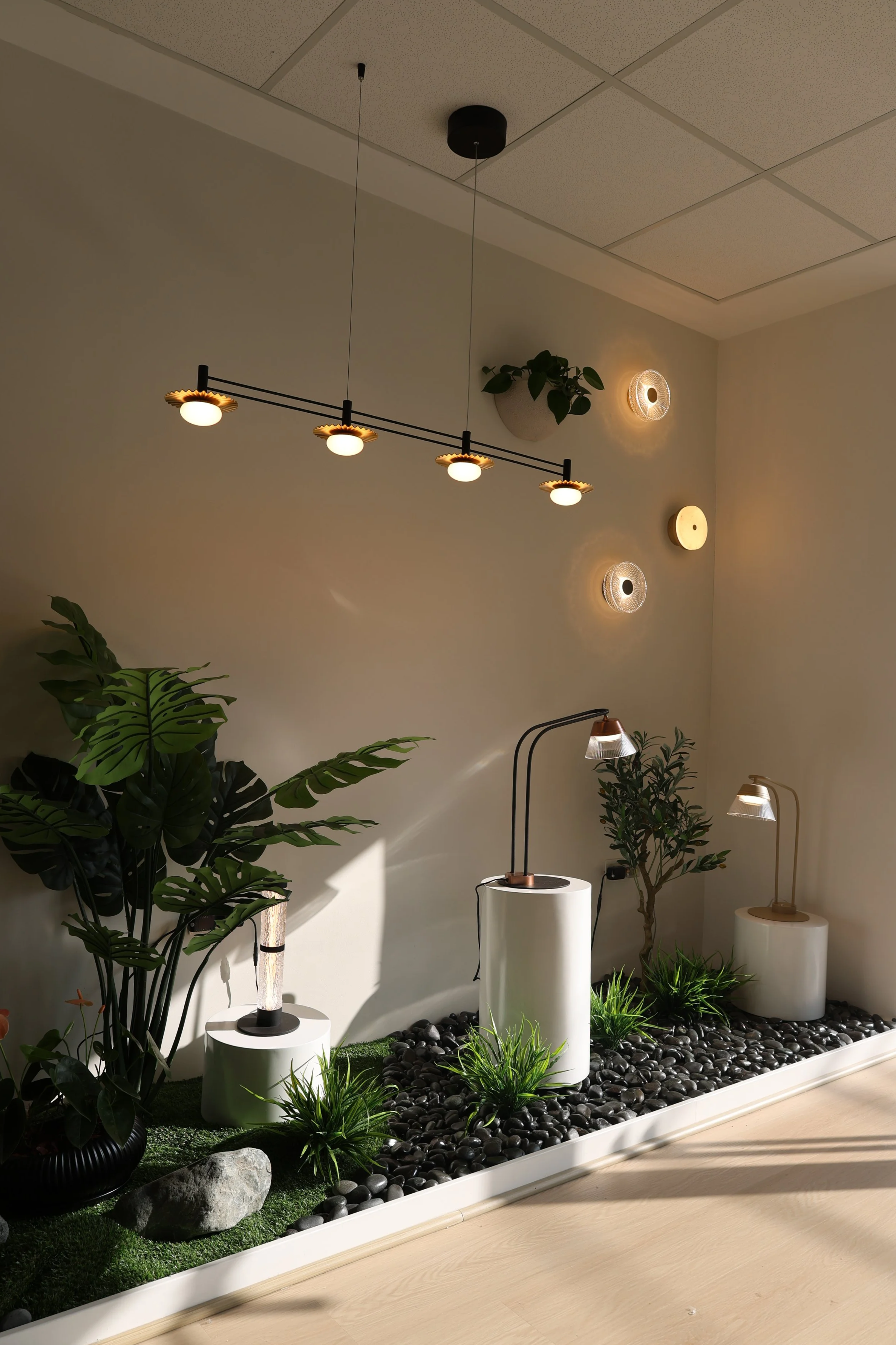 Modern interior with plants, decorative lamps, and a black stone landscape on the floor, illuminated by ceiling and wall lights.