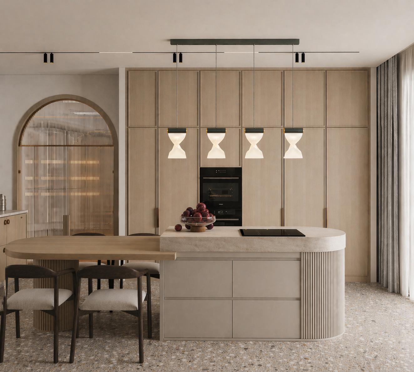 Modern kitchen with a light wood finish, hanging pendant lights, an island with a bowl of red apples, and a built-in oven. There's a dining table with four chairs and a terrace with curtains on the right.
