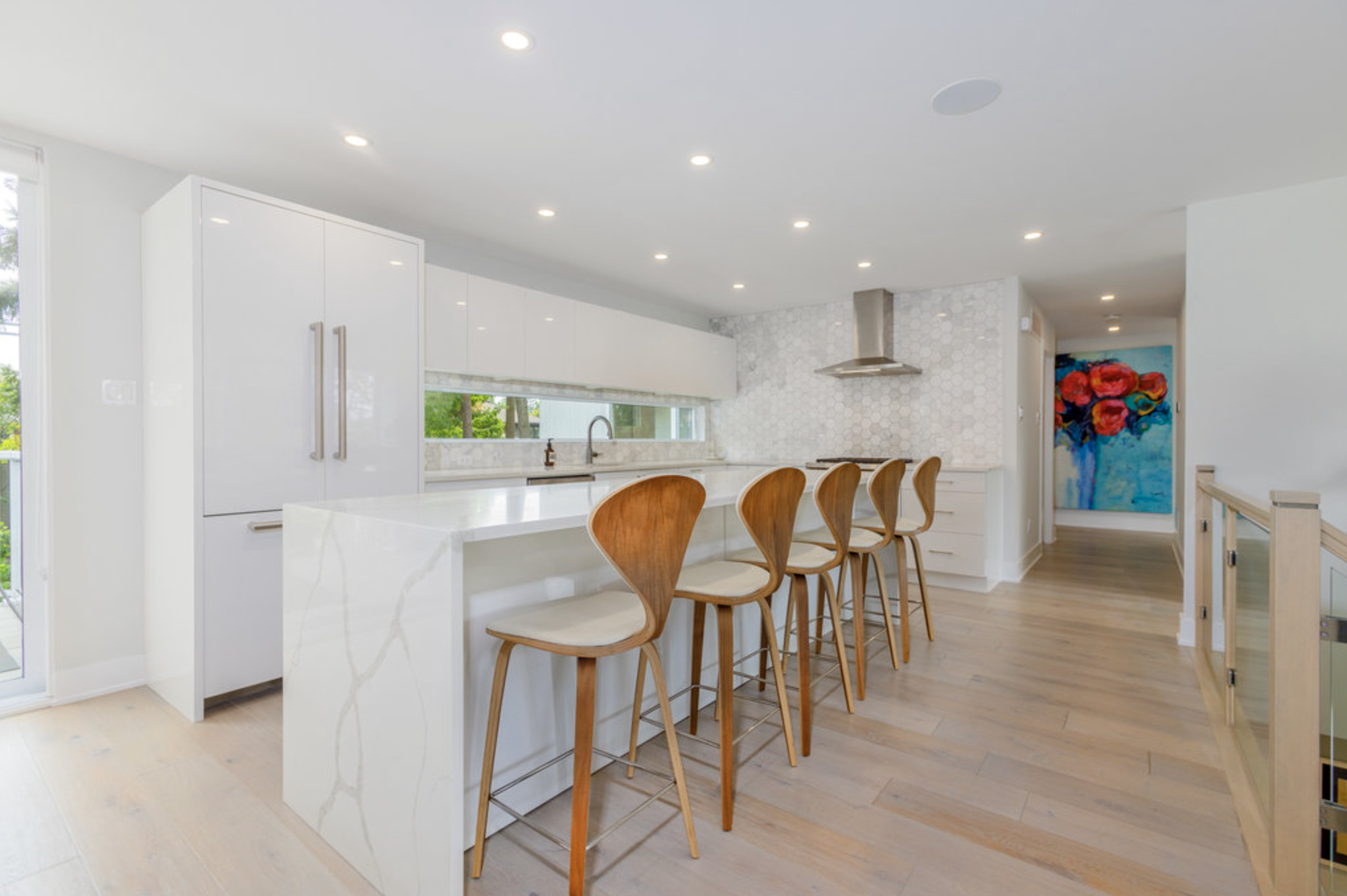 Modern white kitchen with marble island, wooden barstools, and a white backsplash with hexagonal tiles.