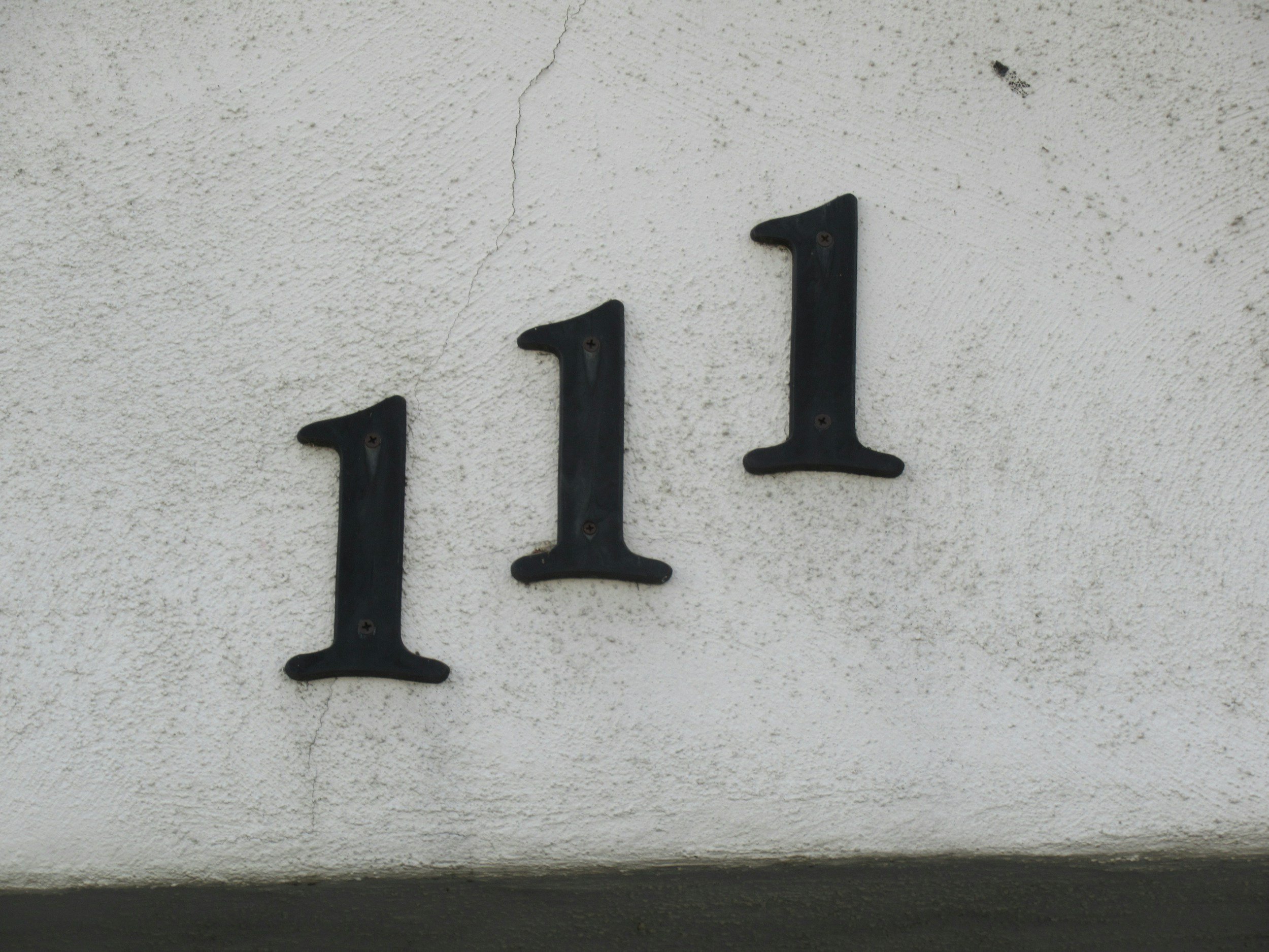 House number 111 mounted on a white textured wall.