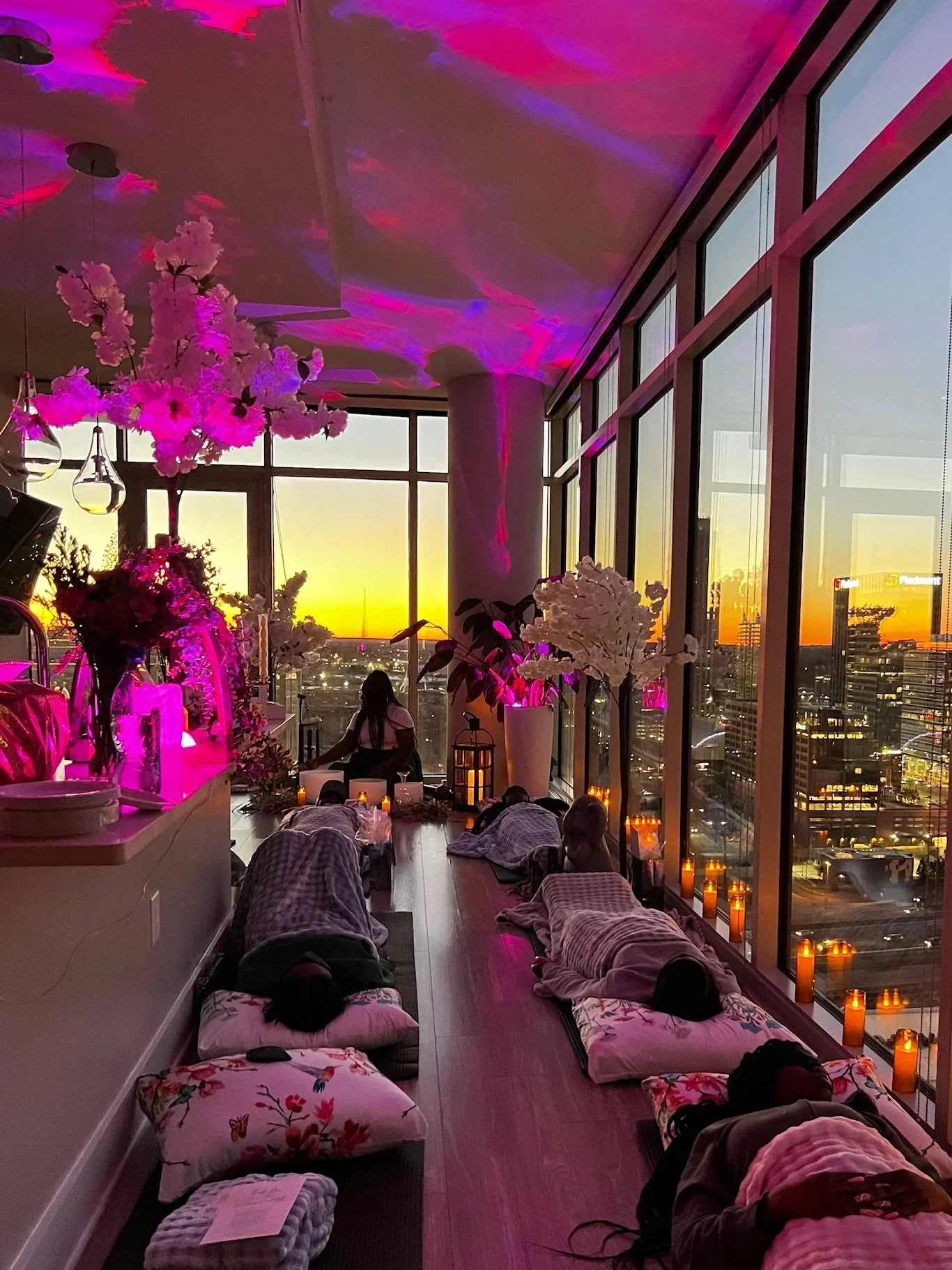 Private sound bath in Atlanta high-rise with sunset city views, guided meditation, crystal singing bowls, candlelight ambiance, and guests resting on mats for deep relaxation and energy healing.