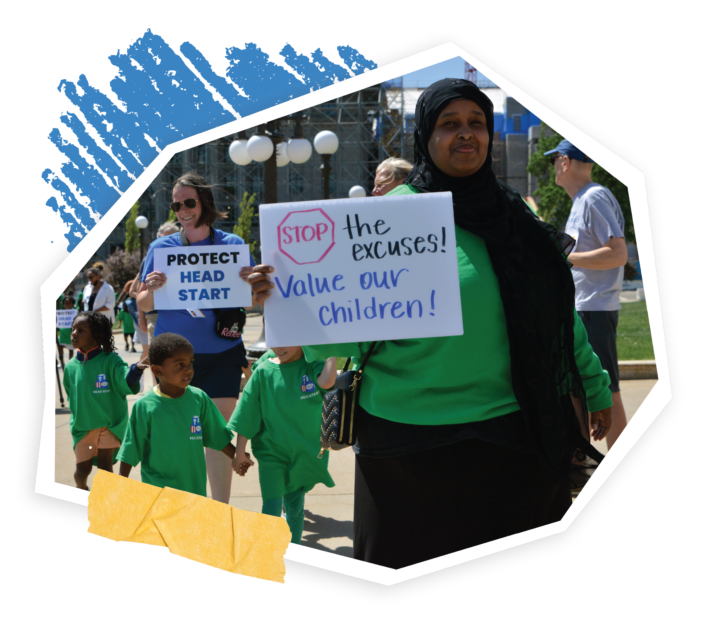 Protesters holding signs that say 'STOP the excuses!', 'PROTECT HEAD START', and 'Value our children', gathered outdoors in a park with city buildings in the background.