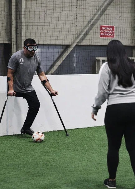Person with crutches playing soccer indoors while a woman watches.