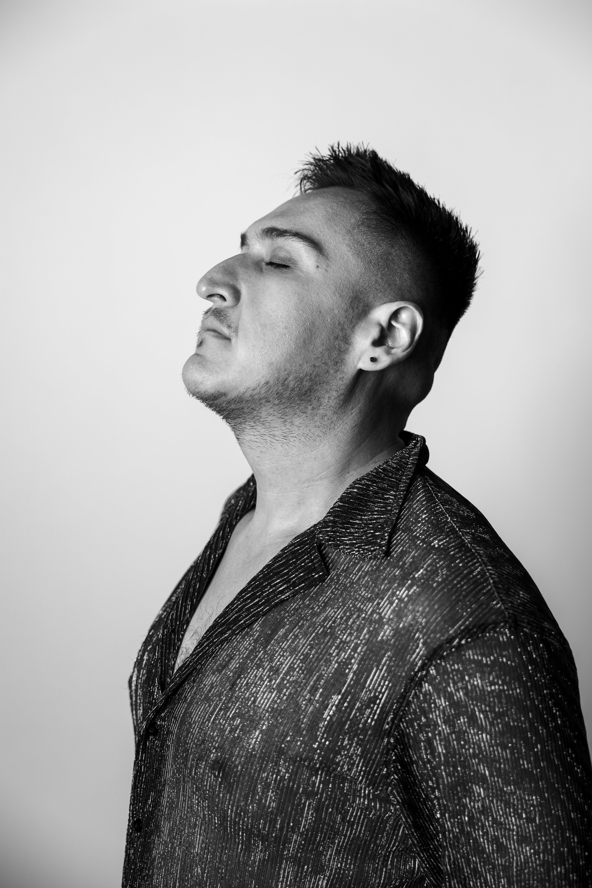 Black and white portrait of a man with nose tilted upward and eyes closed, wearing a textured shirt.