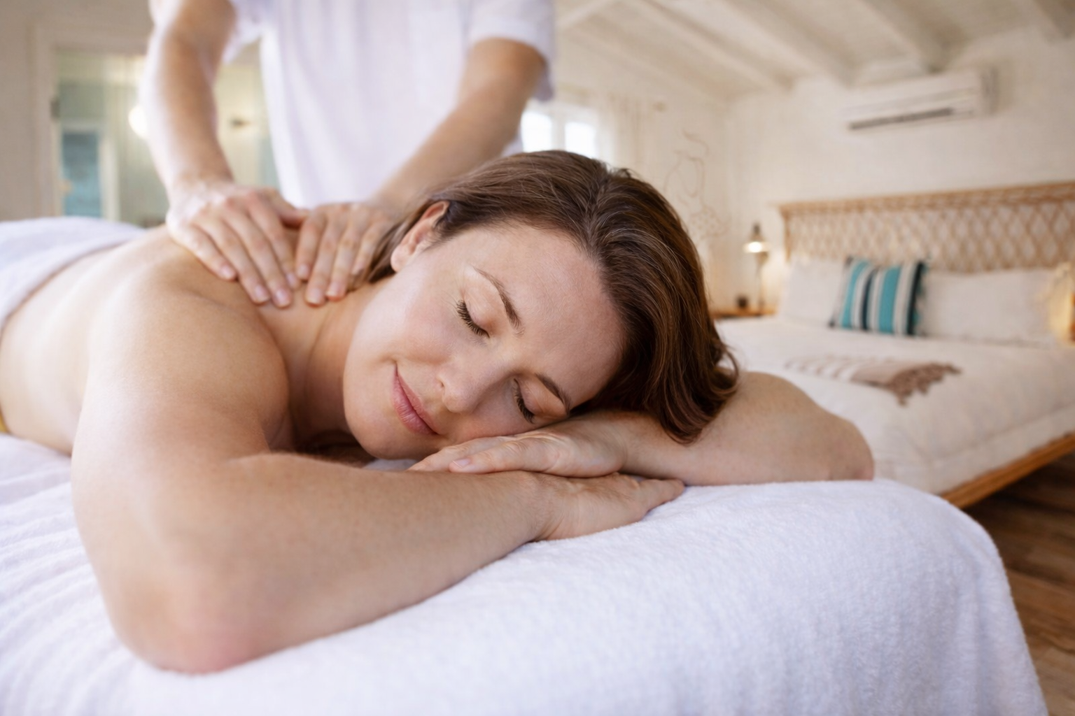 A woman receiving a massage while lying face down on a bed in a cozy bedroom.