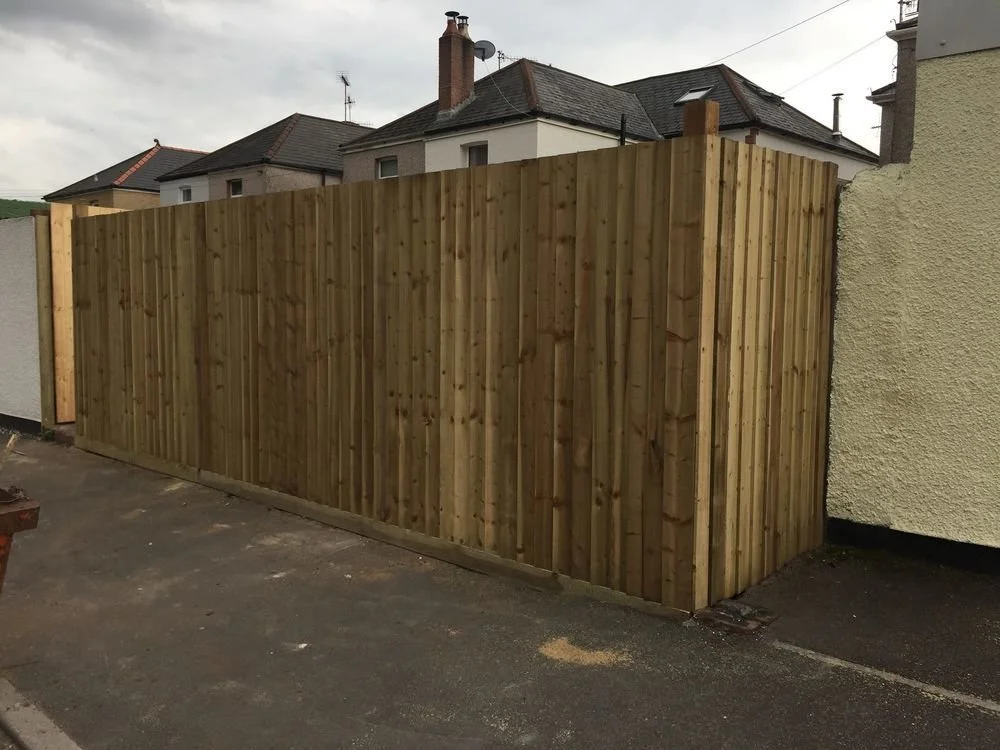 Wooden privacy fence surrounding a backyard near houses with brick chimneys.