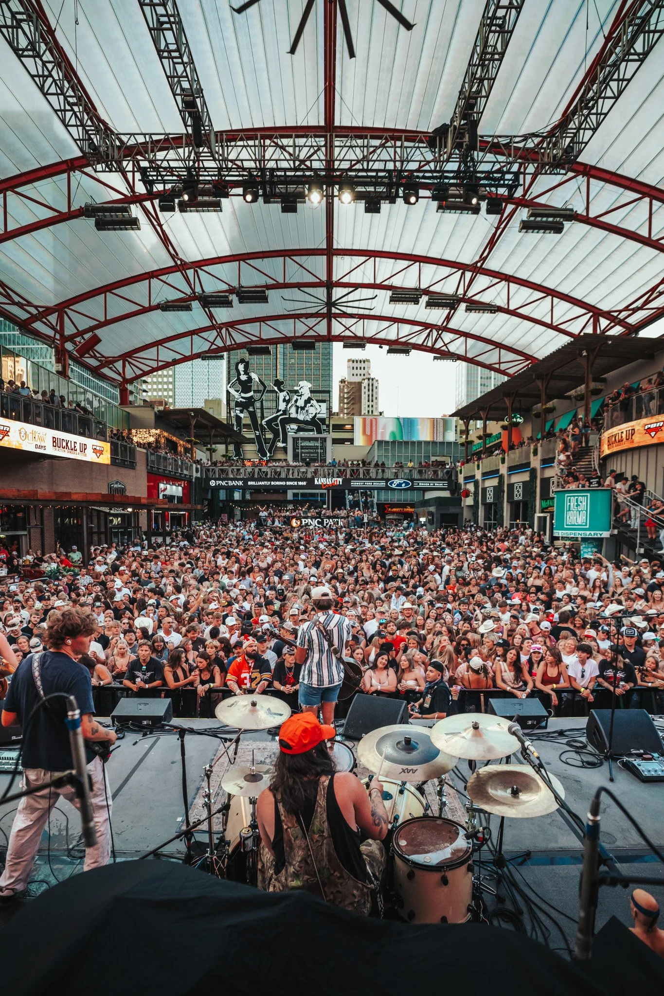 Band playing in front of a large crowd in a covered events space.