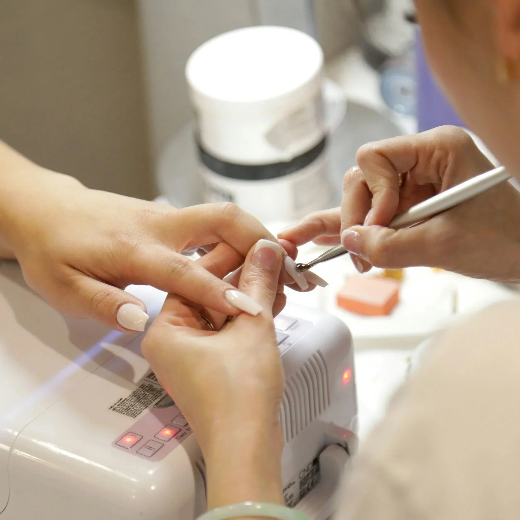 Manicurist applying white nail polish to a customer's fingernails using a small brush.