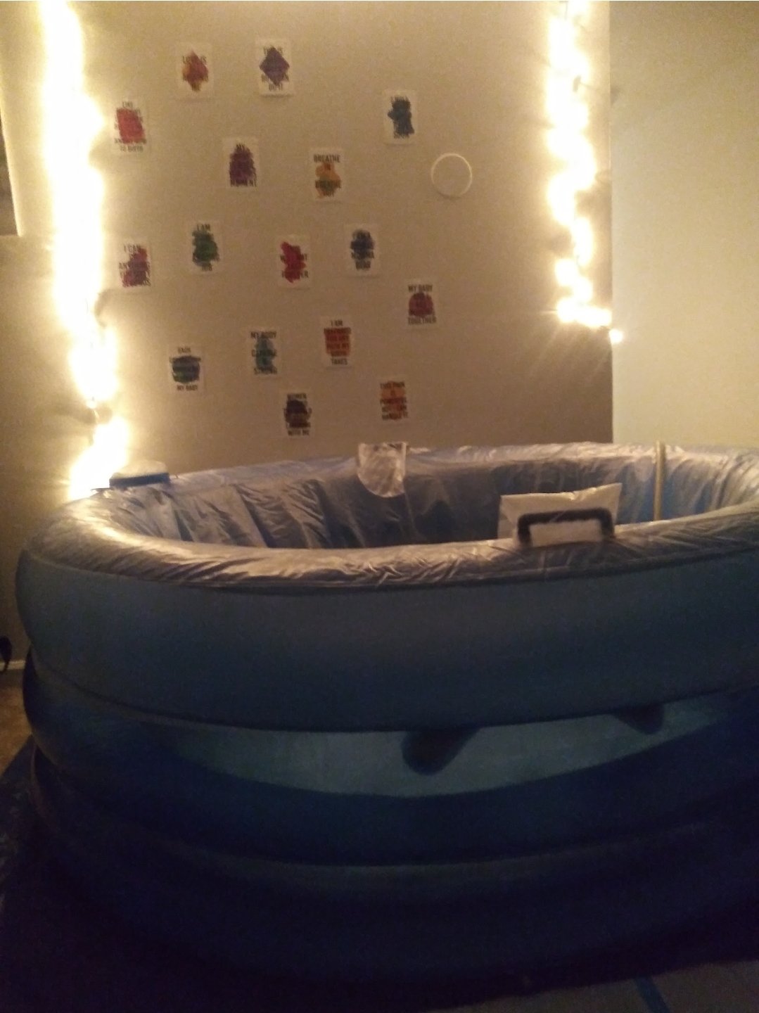 Indoor scene with an inflatable pool in a living room, decorated with holiday-themed paper cutouts on the wall and string lights along the wall.