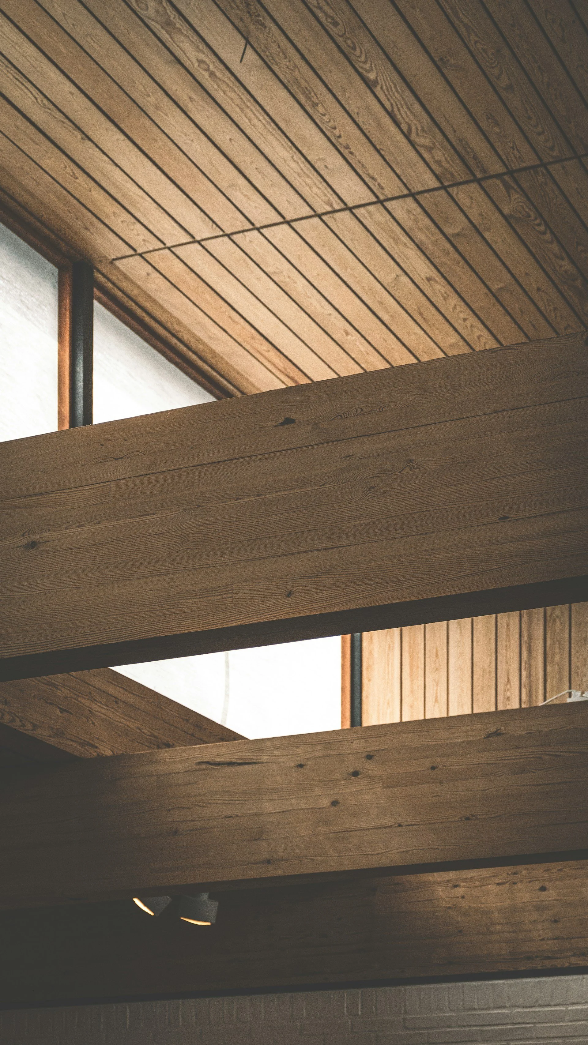 Interior ceiling with wooden panels and beams, including natural light coming through from windows.