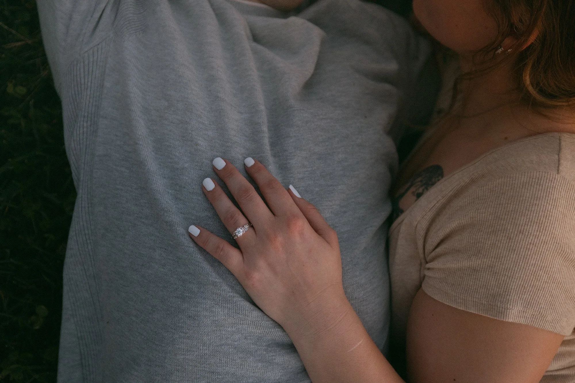 A woman with a wedding ring resting her hand on a person's gray t-shirt, showing her white manicured nails and part of her face and shoulder.