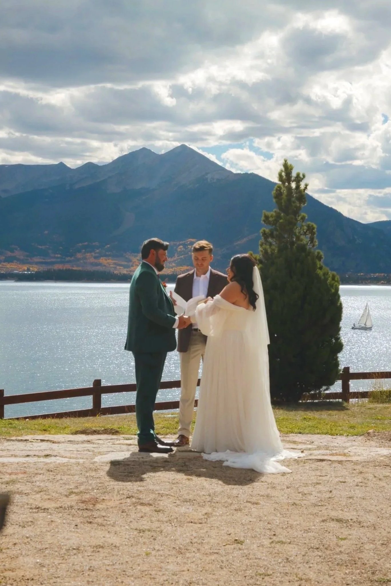 A wedding ceremony taking place near Dillon Lake in Colorado, with mountains in the background, officiant and bride and groom exchanging vows.