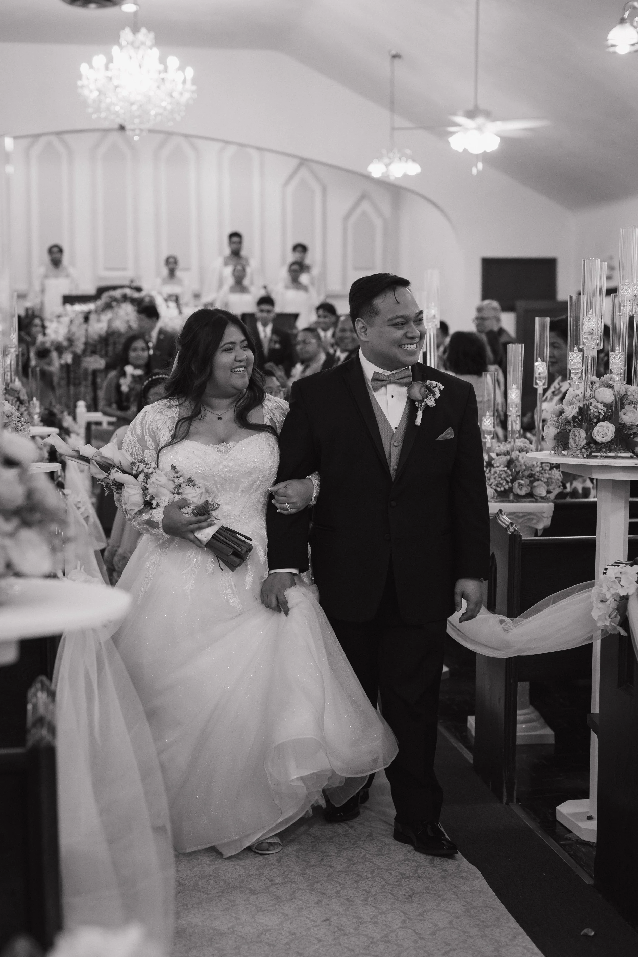 A newlywed couple walking down the aisle during their wedding ceremony in a church, surrounded by guests and floral decorations.