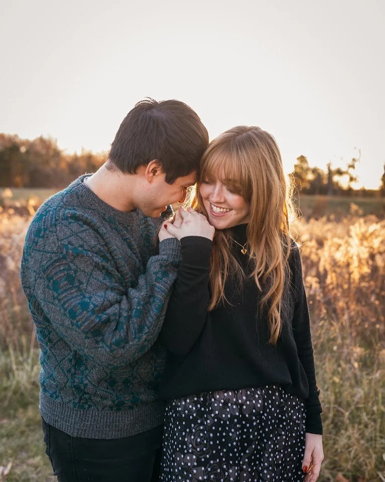 A young couple sharing a tender moment outdoors during sunset, holding hands and smiling.