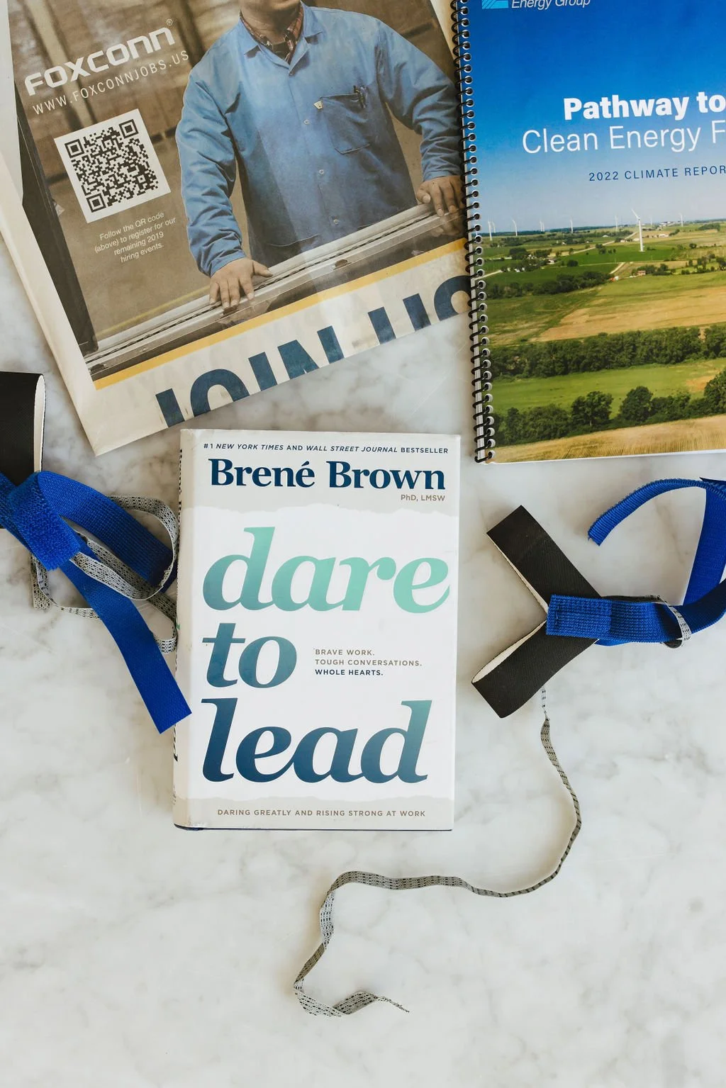 Books, lanyards, and a magazine on a white marble surface. The books include 'Dare to Lead' by Brené Brown, and others related to energy and climate reports.