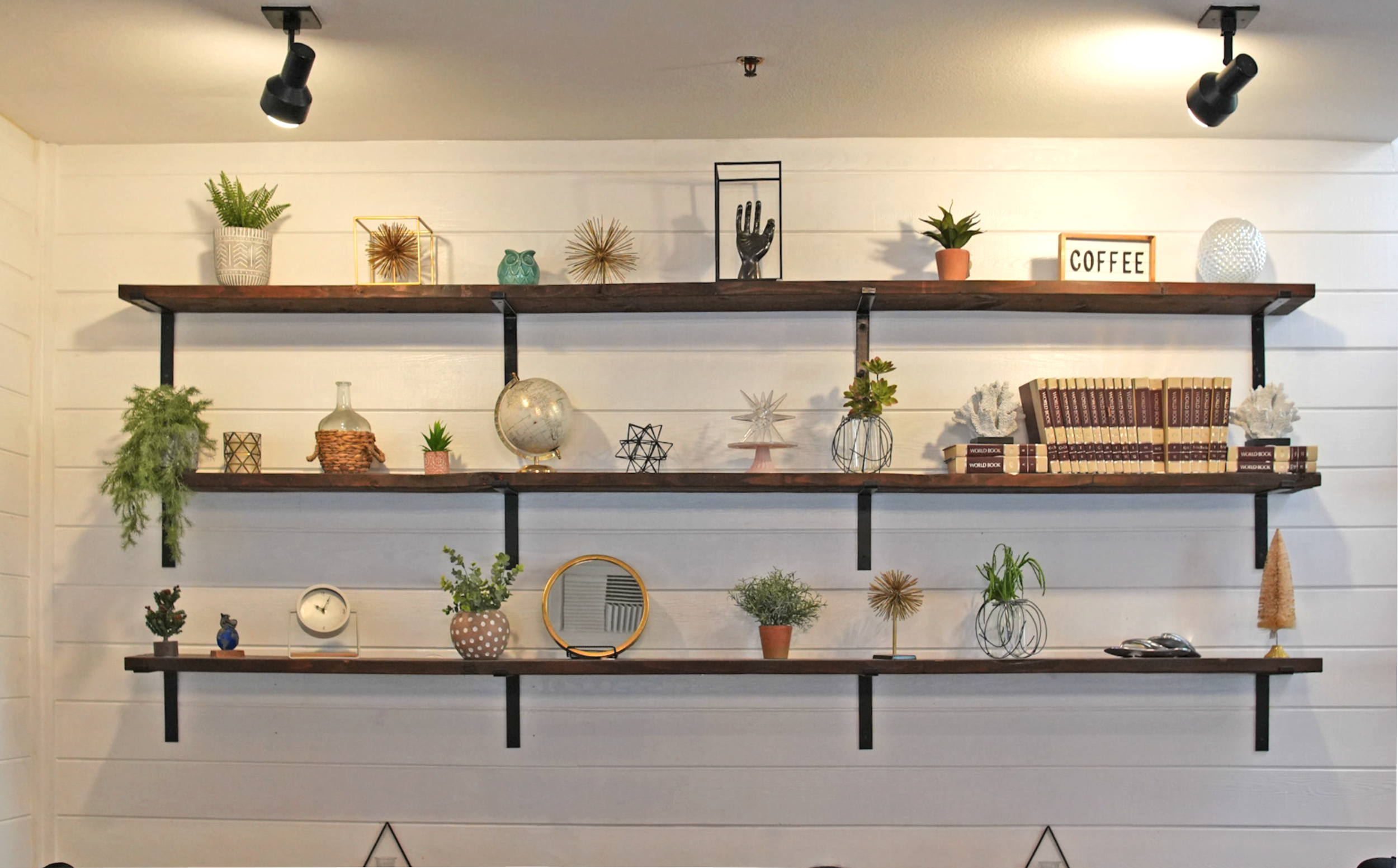 Decorative shelves with plants, books, and ornaments against a white wall in a cozy interior.