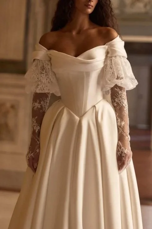 Woman in a vintage-style off-the-shoulder wedding dress with lace sleeves in an elegant room.