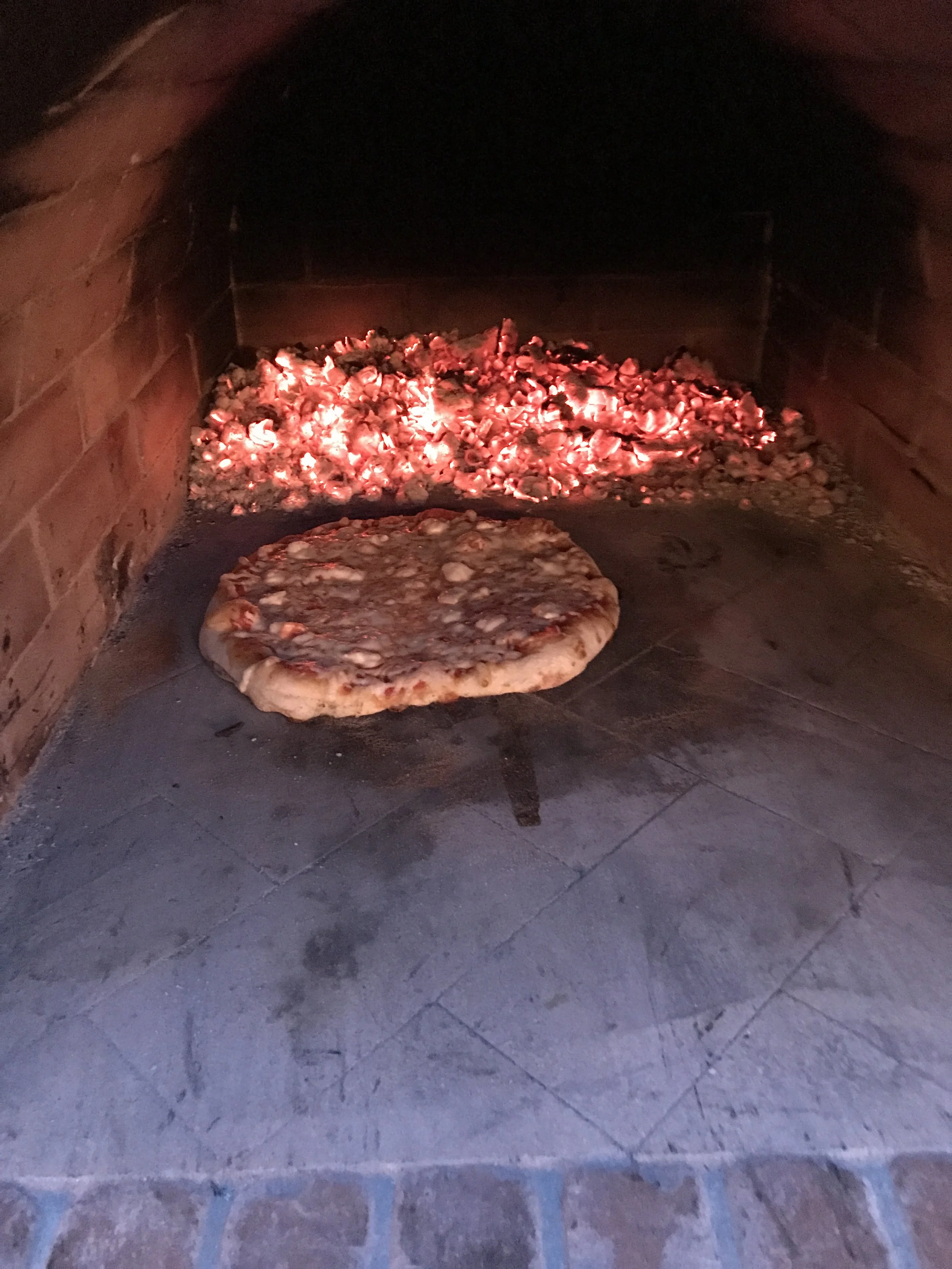 Pizza being baked in a wood-fired oven with glowing embers inside.