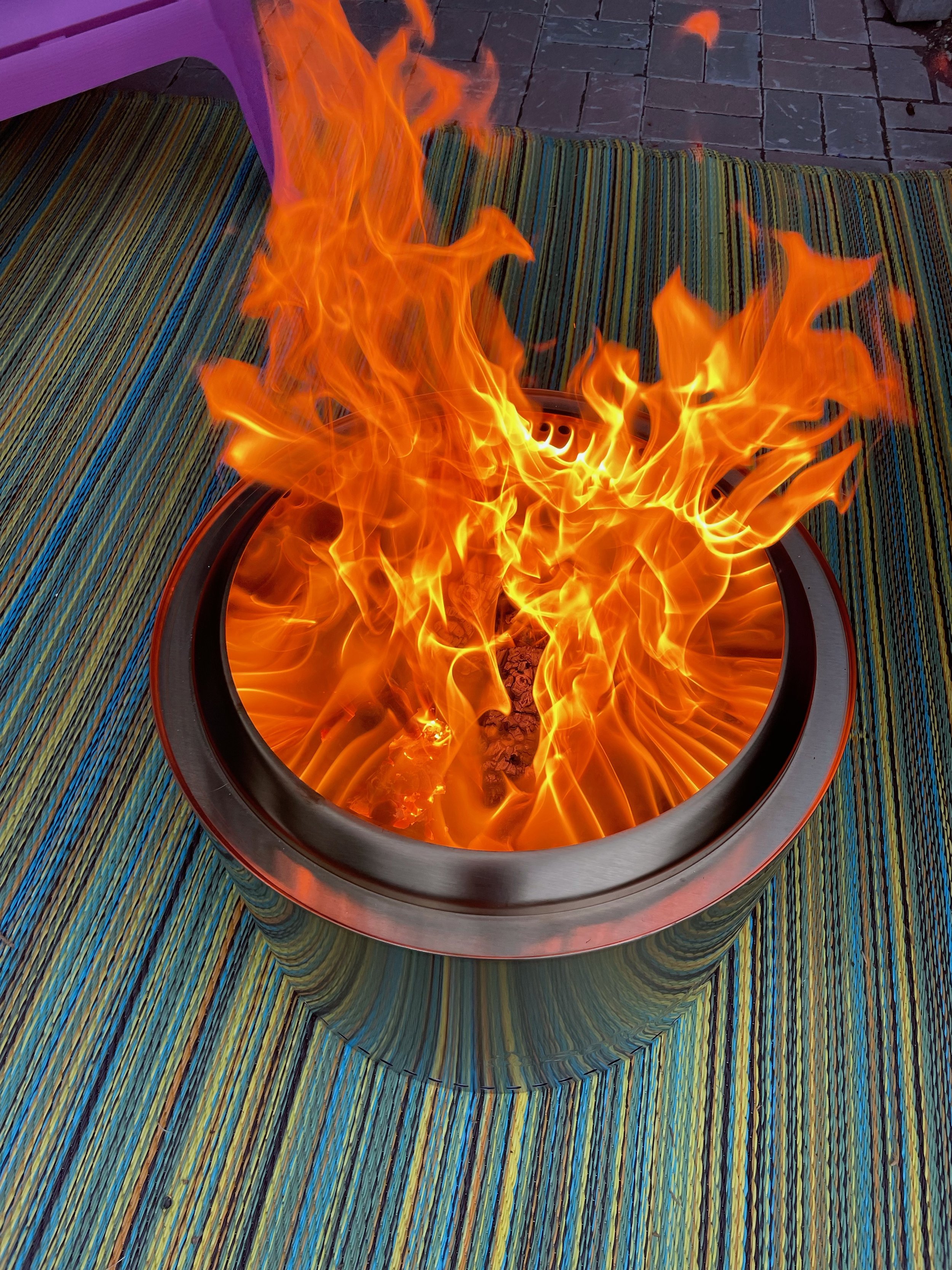 A fire burning in a modern fire pit on a multicolored textured outdoor rug.