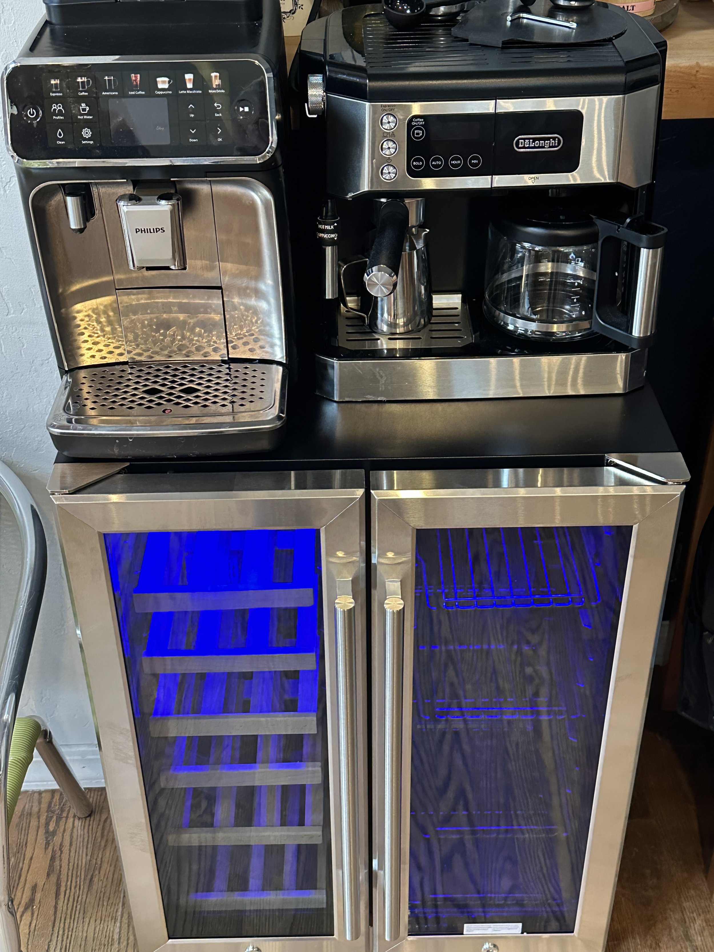 A countertop with a built-in coffee machine, a coffee maker with a glass carafe, and a small wine fridge with blue lighting and glass doors.