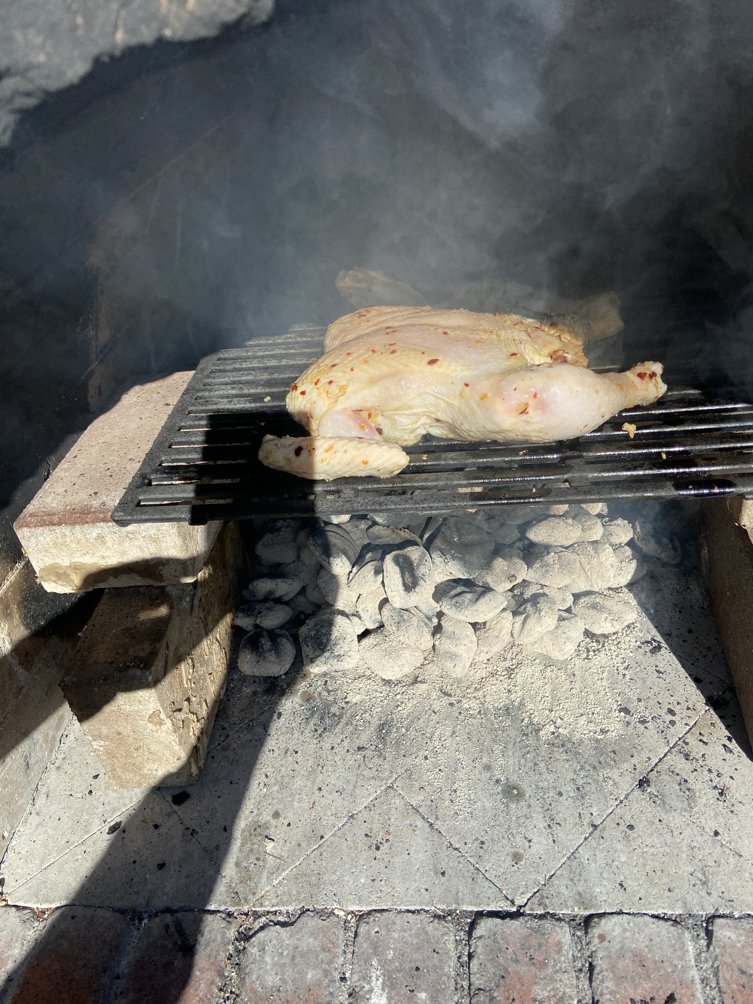 Chicken cooking on a grill inside an outdoor brick oven.