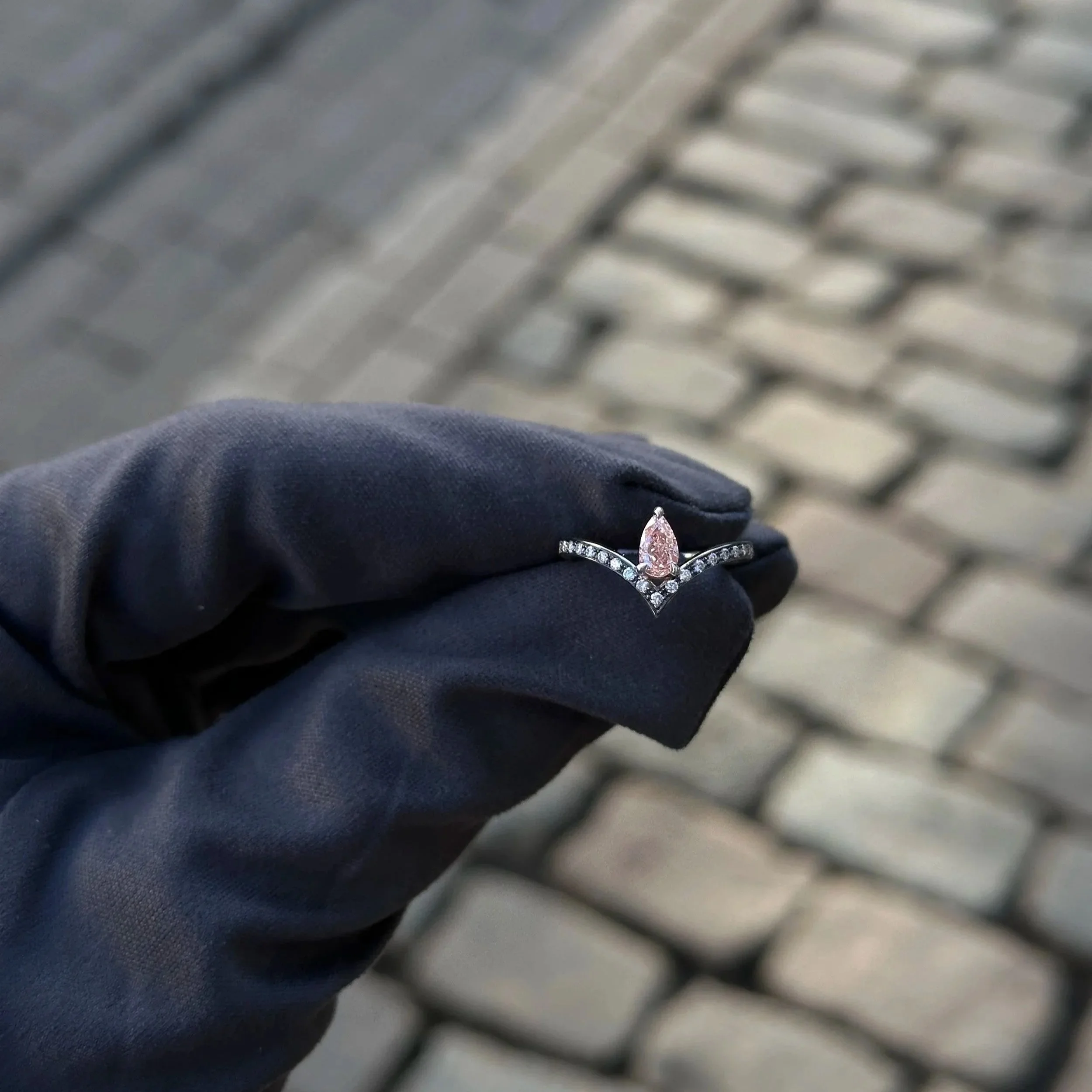 Close up of pink pear shaped diamond ring. Accentuated with side diamonds, polished with black rhodium.