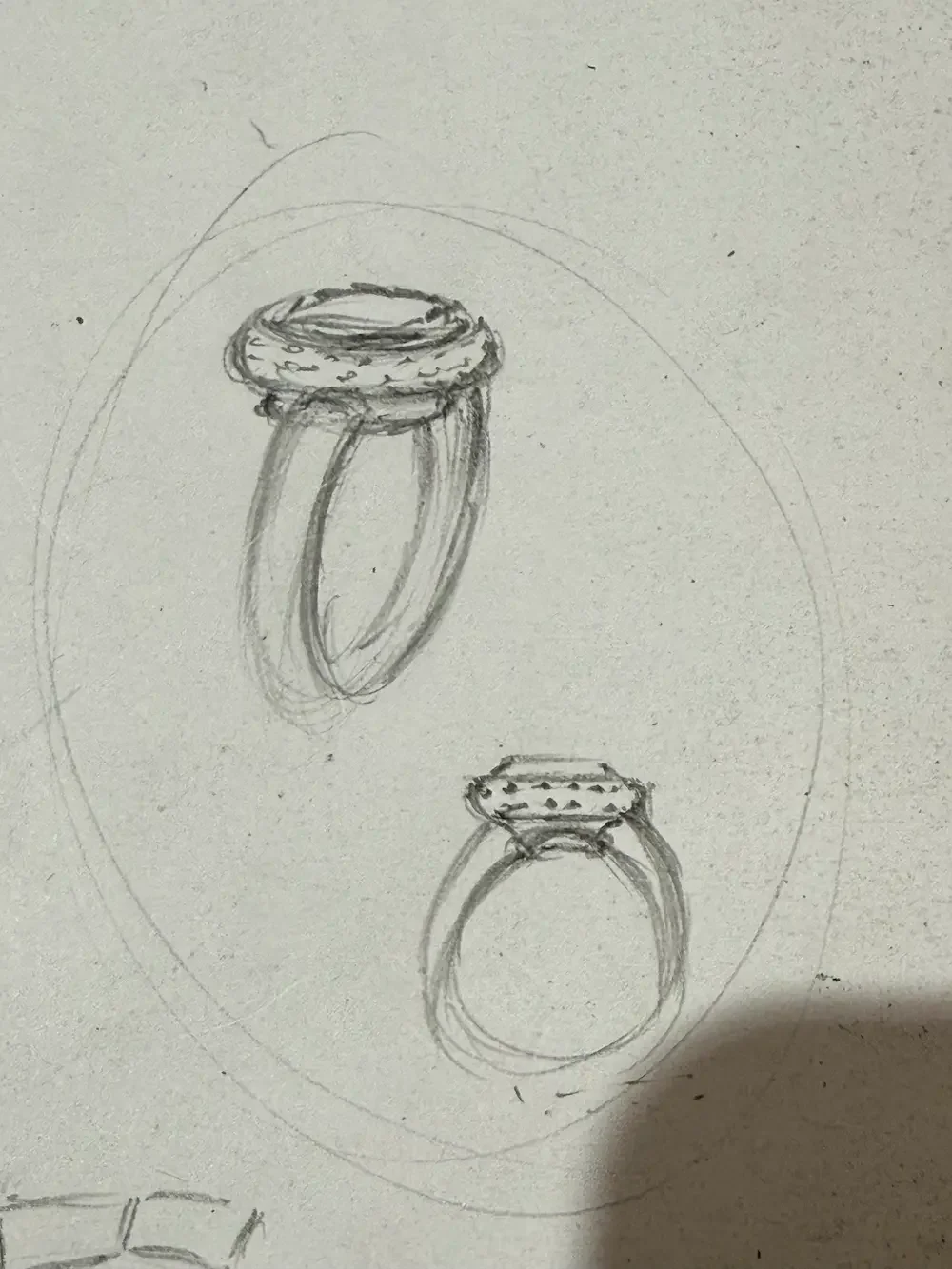 Hand-drawn sketch of two rings viewed from different angles, one with a large oval gemstone and the other plain.