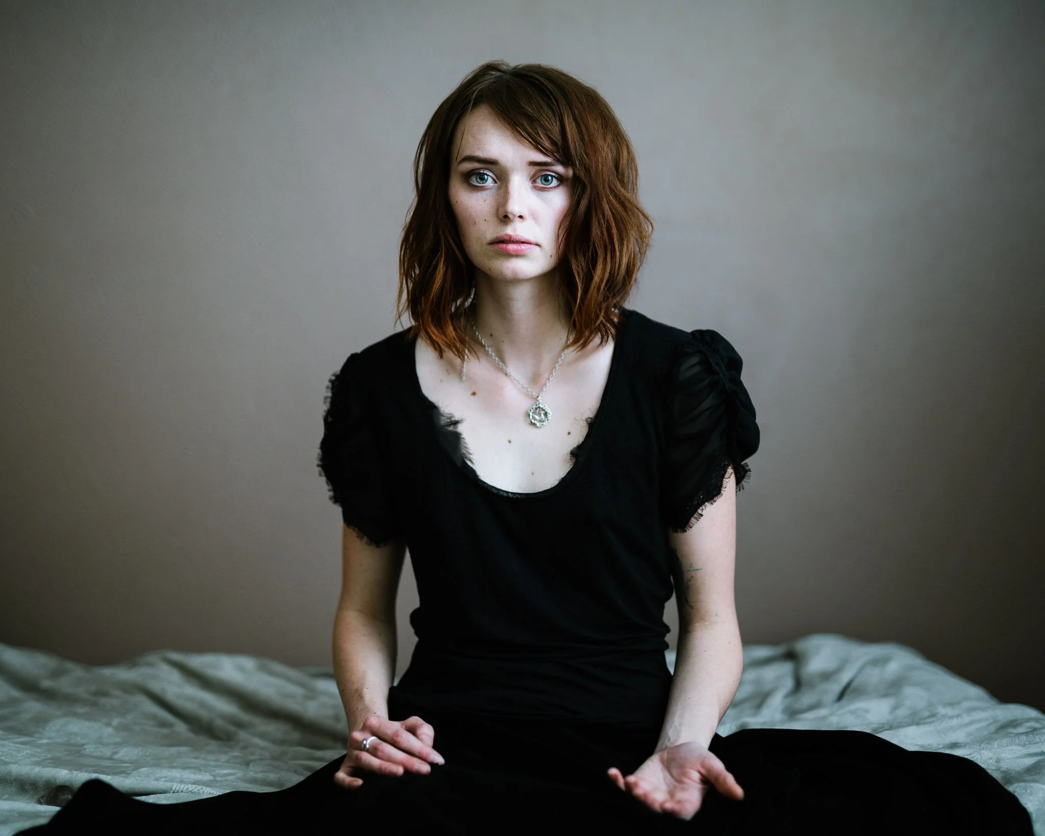 Portrait of a woman with pale skin and a black dress with a haunted expression. She has fears that voices in her head are the beginning of an inheretance of her grandmother's schizophrenia.