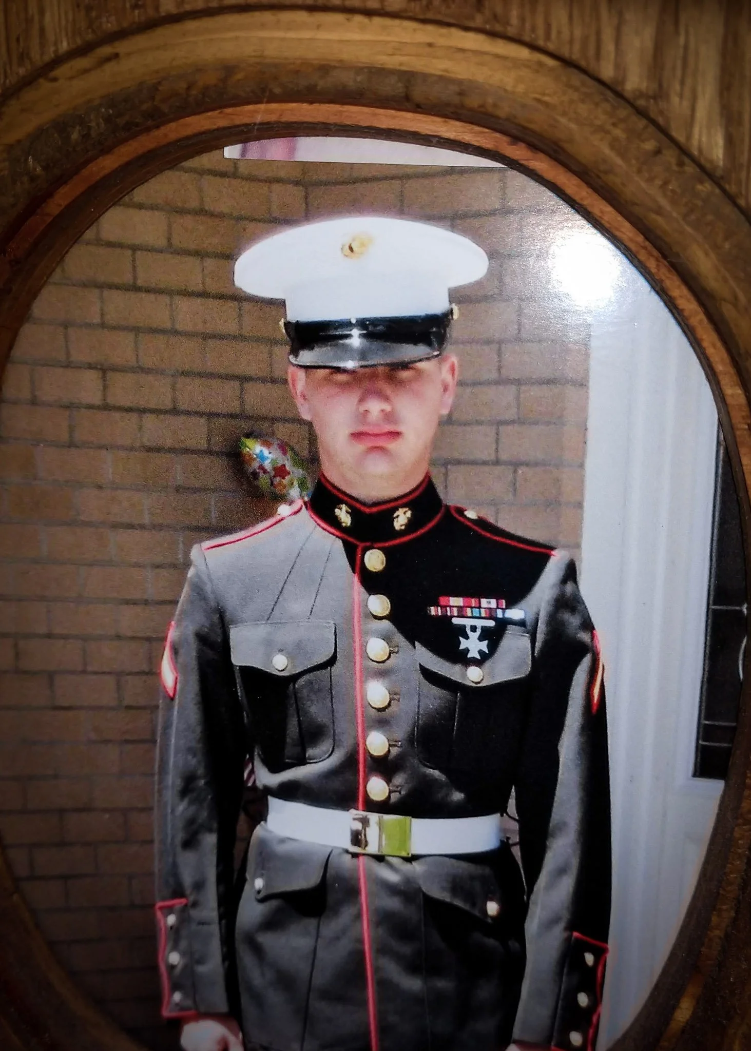 Detail of an amateur photograph of a young Marine in his Class A uniform, tucked into an oval wooden frame.