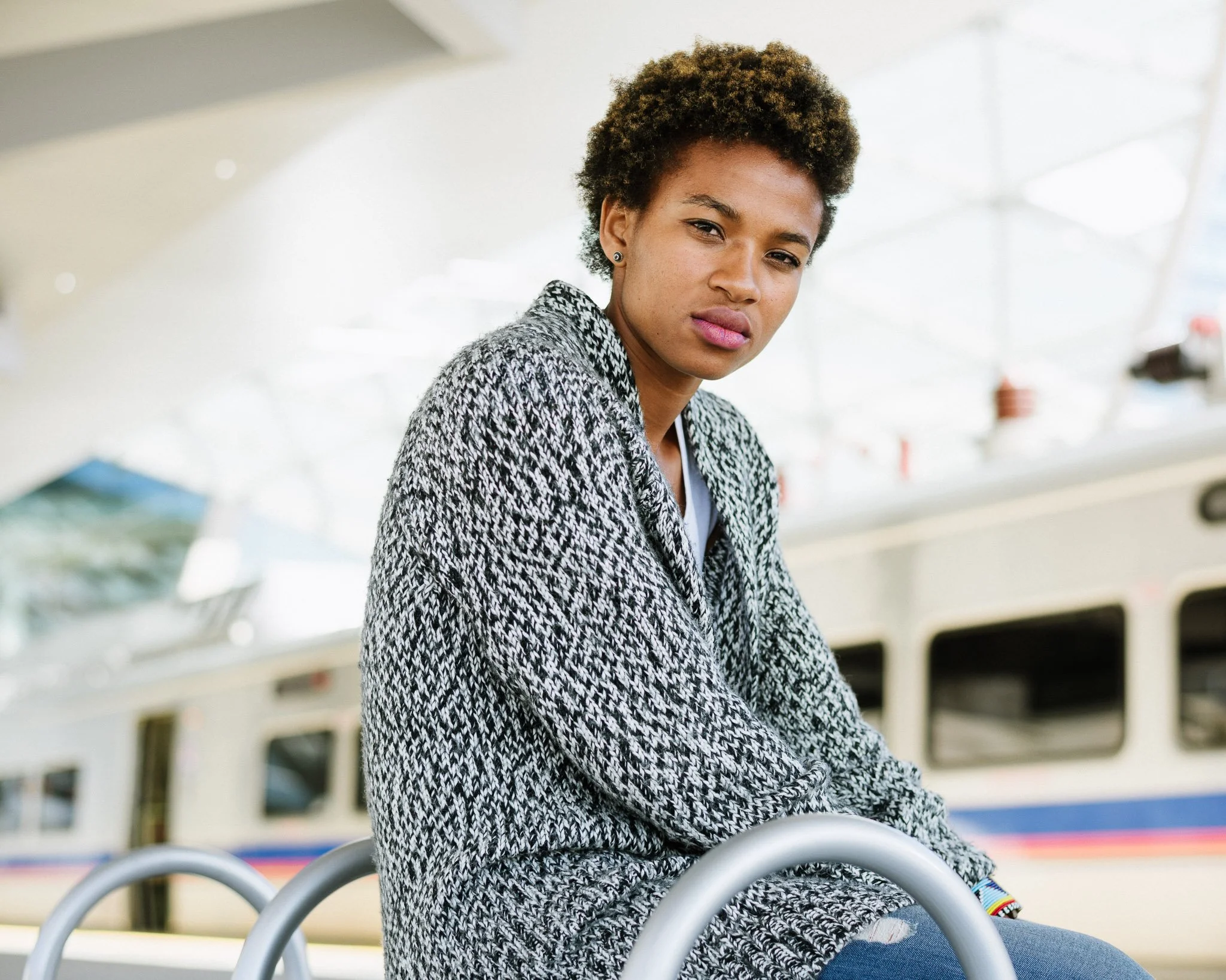High-key image of South African woman waiting on the train platform of the Denver airport in a course black and white sweater, background defocused, looking directly at the viewer.
