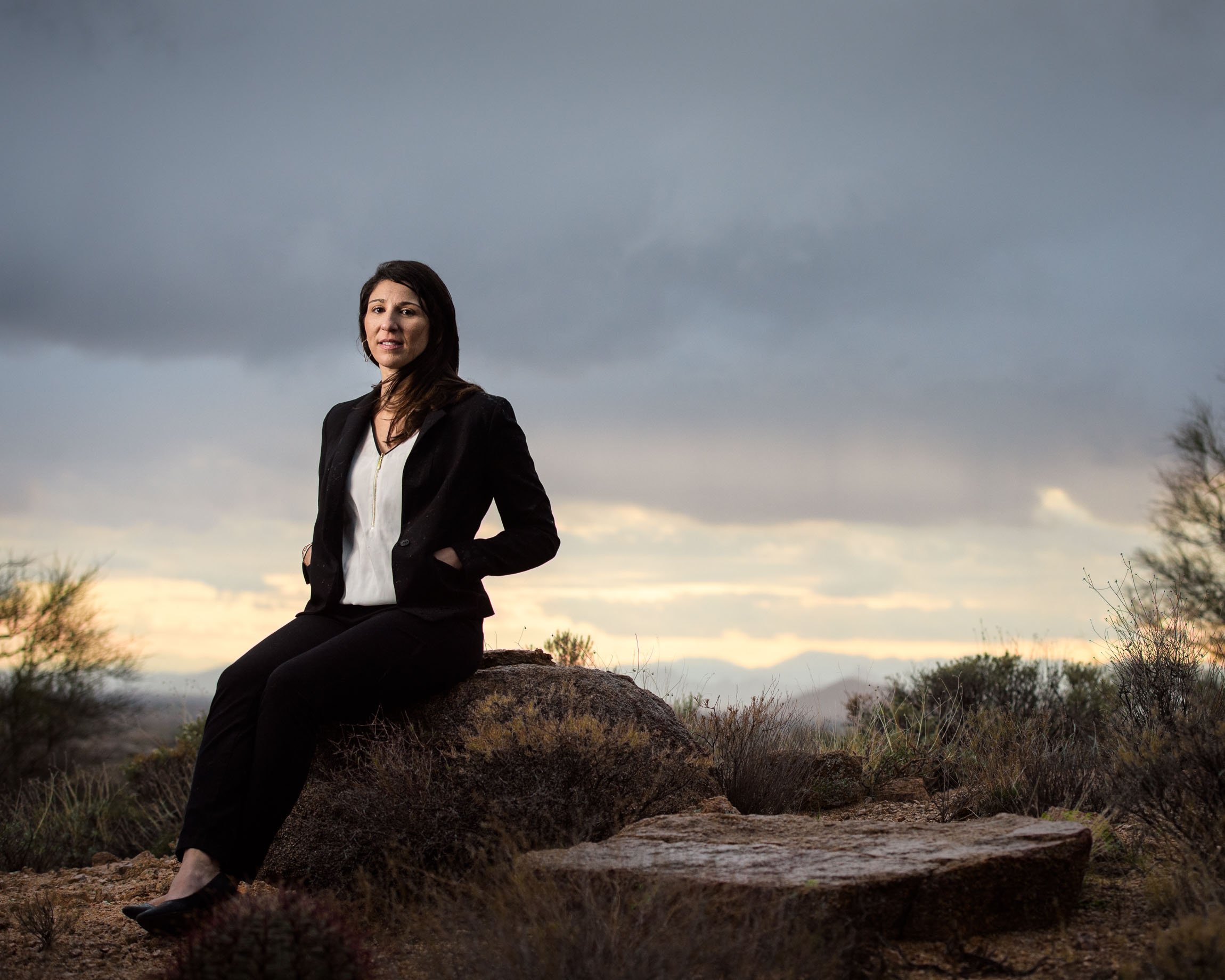 Portrait of architect Andrea Lucarelli in a black blazer in the Arizona desert on a gloomy stormy afternoon, Rembrandt lighting, the breeze of a coming storm blowing her long hair.