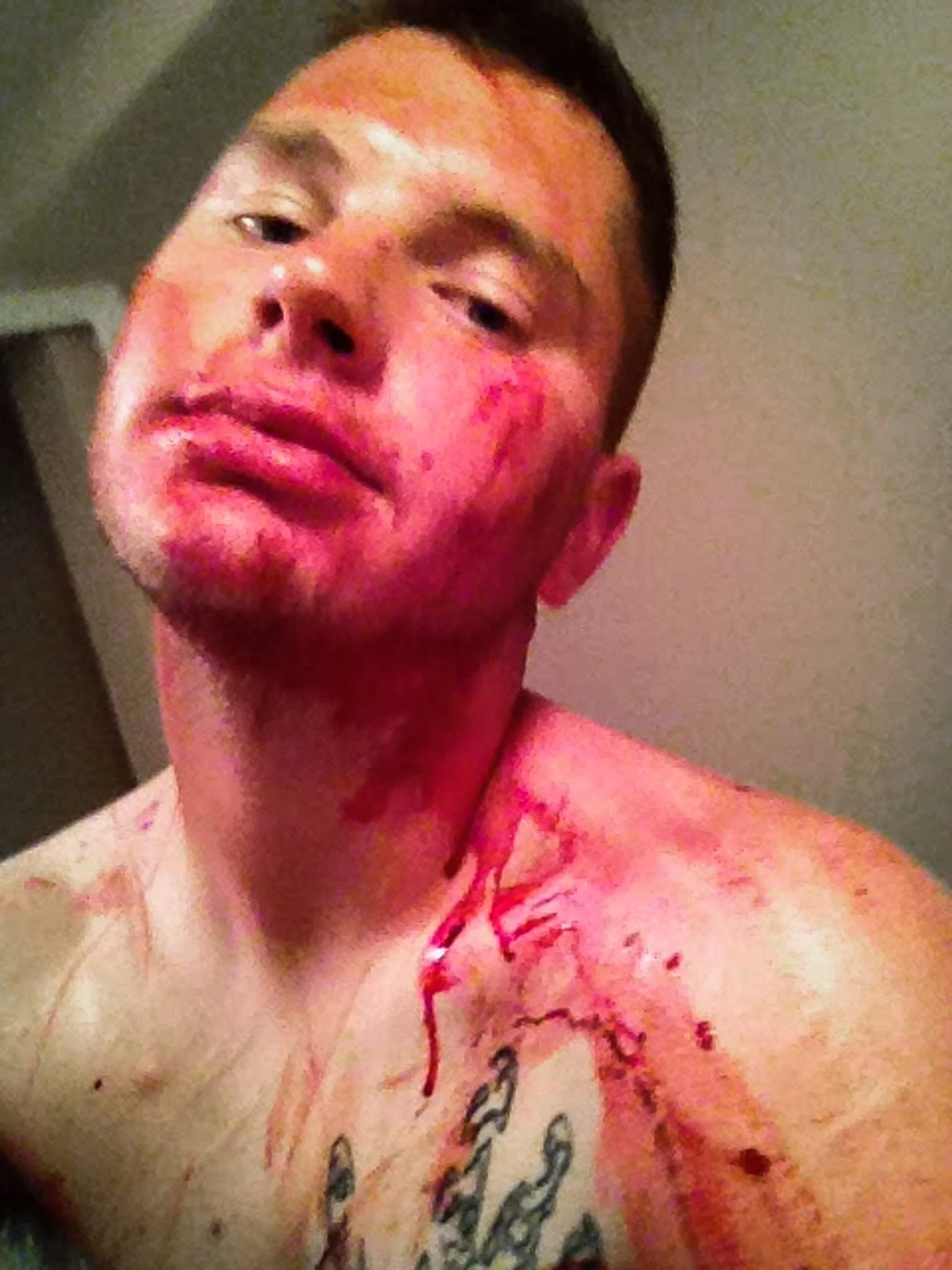 Young discharged marine, his  face, heck, and shoulders dripping with blood from cuts he has made to his own body. A selfie, taken in his bathroom.