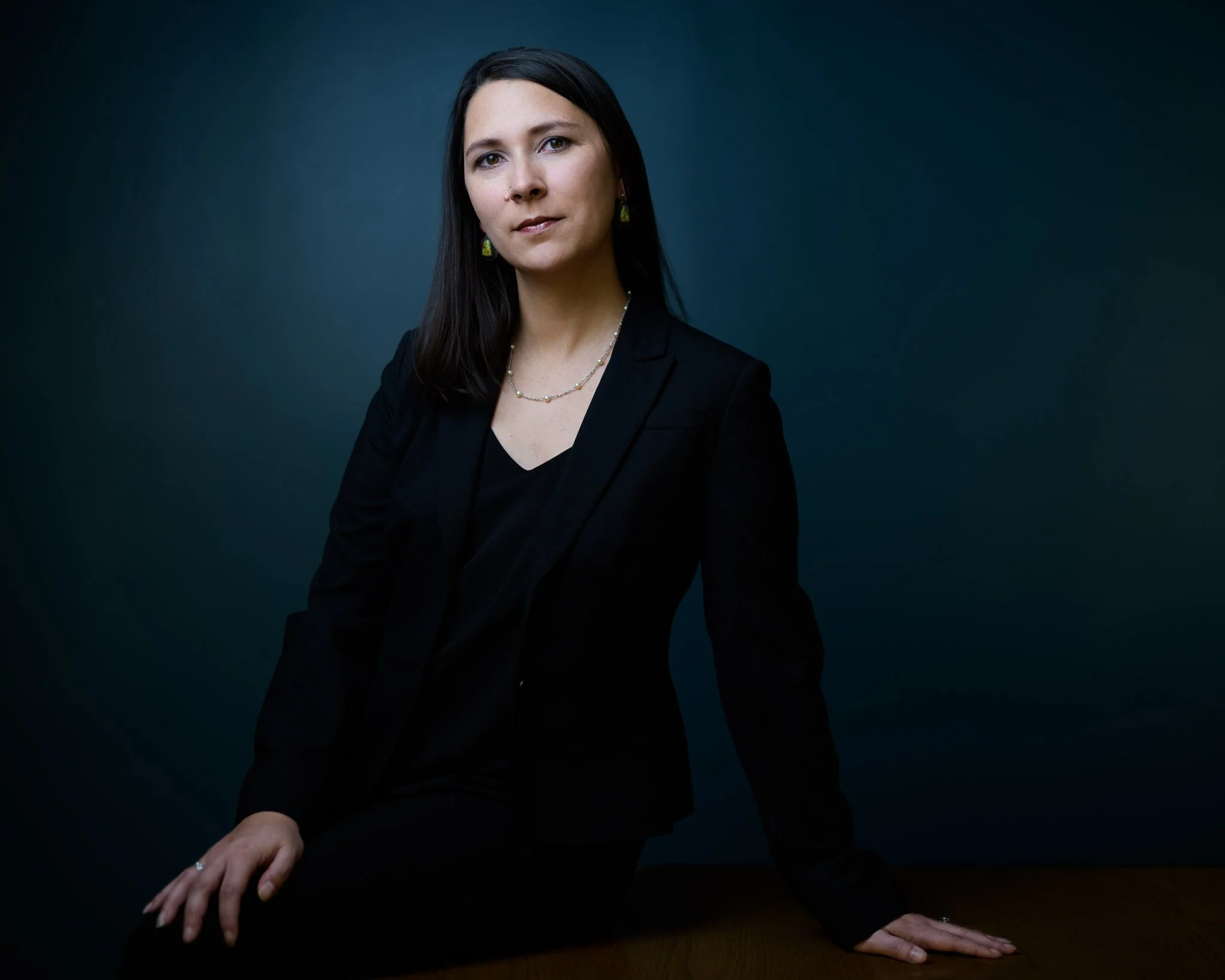 Corporate portrait with blue tone of young executive Latina in black against a cobalt background projecting vision and approachability.