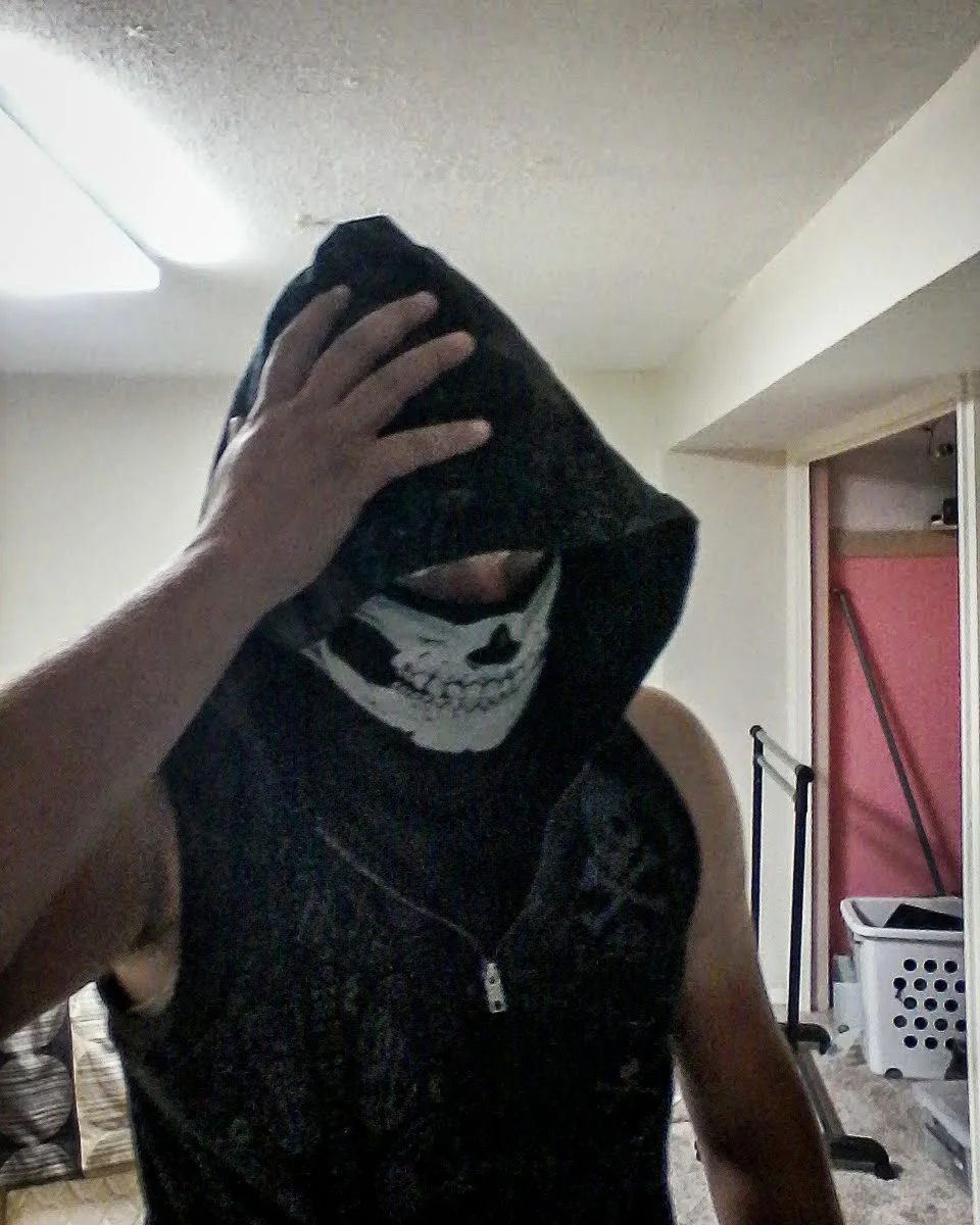 Former Marine's selfie wearing a sleeveless black hoodie and a skeleton mask in a basement laundry room.