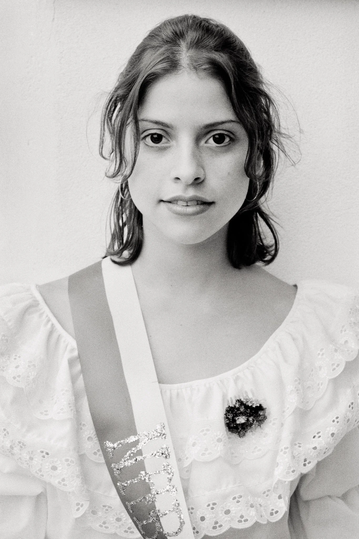 Simple black and white portrait of a Colombian beauty queen in a frilly white top, an open, fresh gaze. Her hair is simple, she appears to have no makeup. She is the innocent antithesis to the more typical manufactured beauty of such contests.