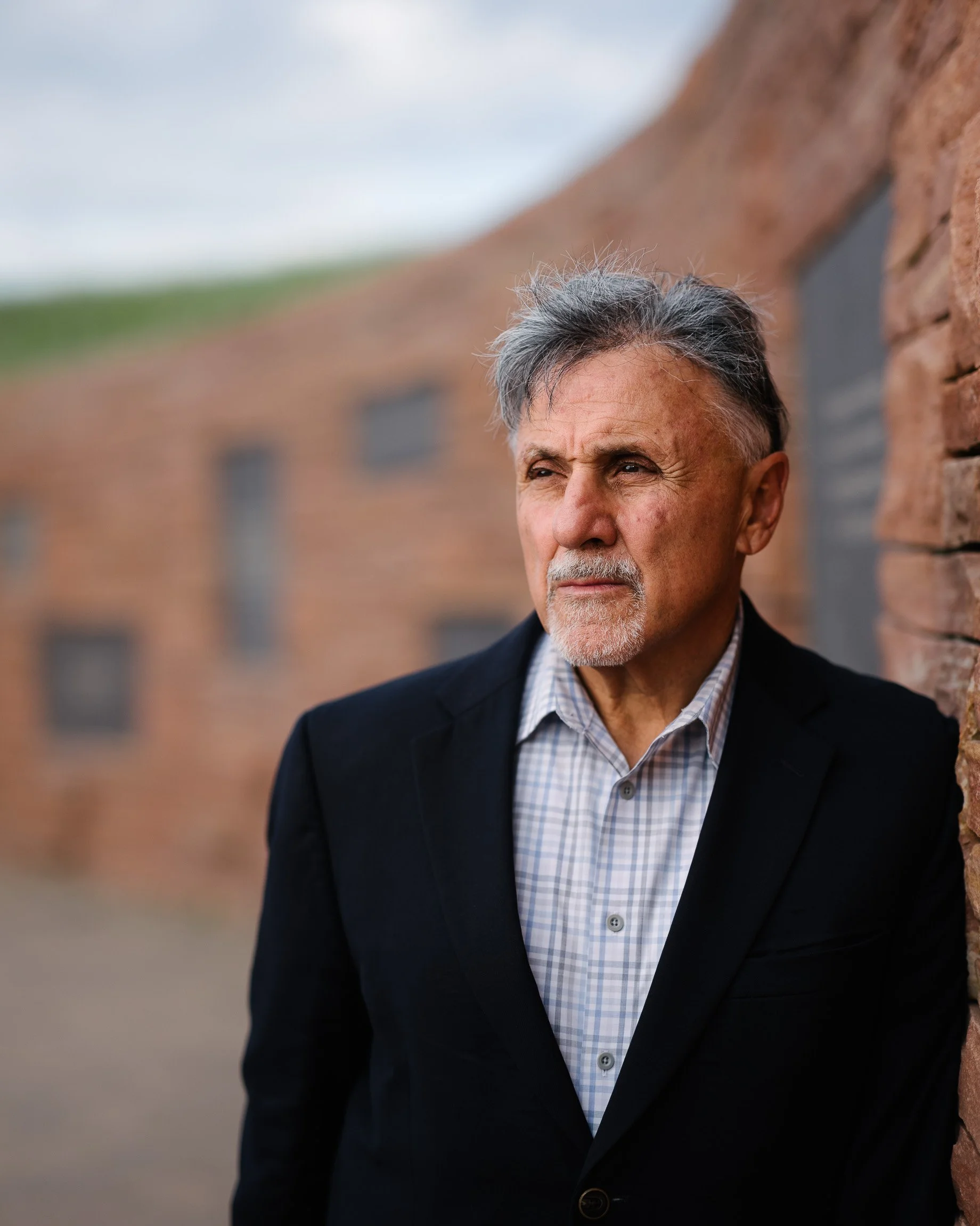 Frank DeAngelis, former principal of Columbine High School, in a checked shirt and blazer leaning against the sunken wall of a memorial to the students and staff killed in the shooting.