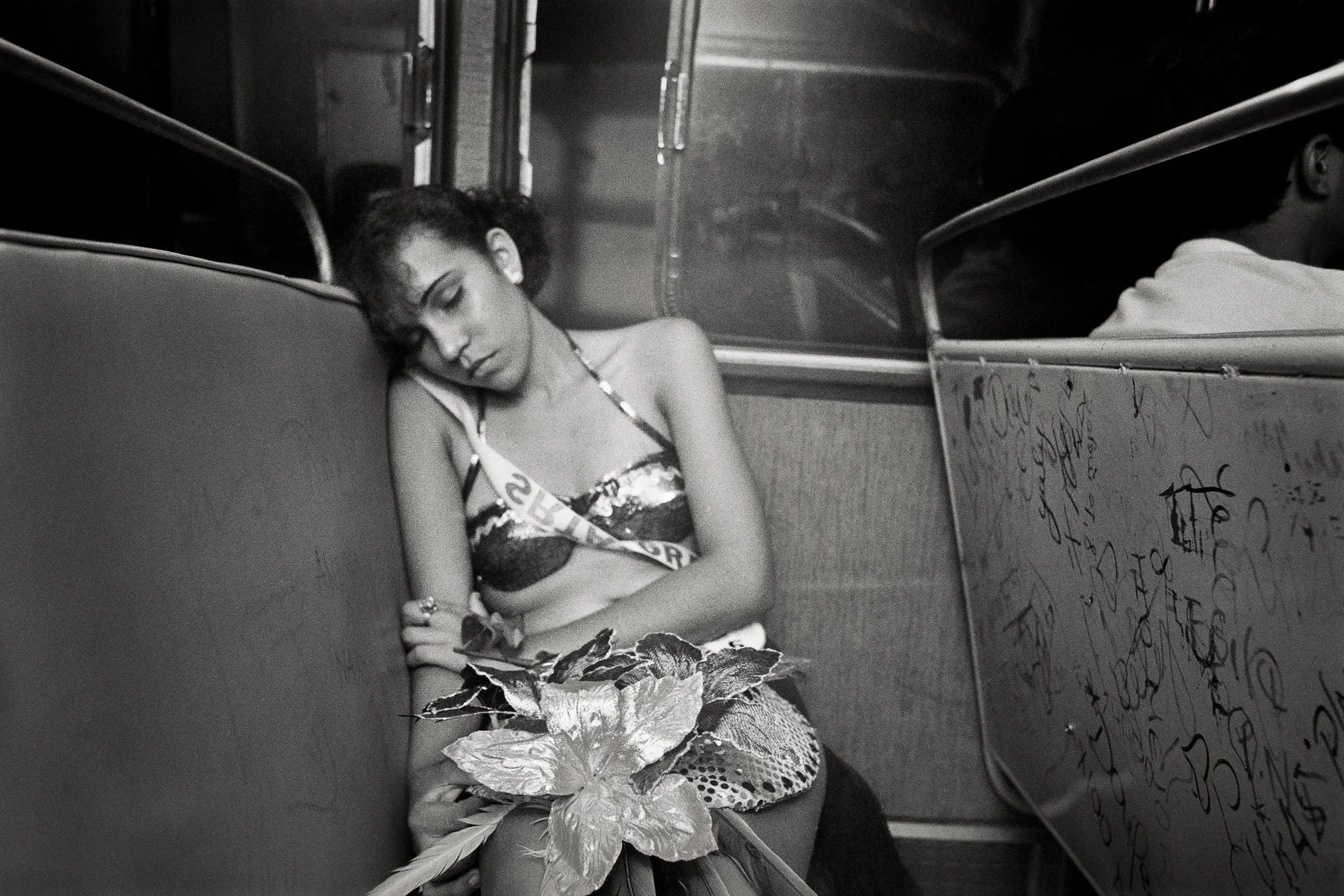 A beauty queen sleeps on a bus in the early morning hours, still in her bikini and sash, exhausted after a long day.