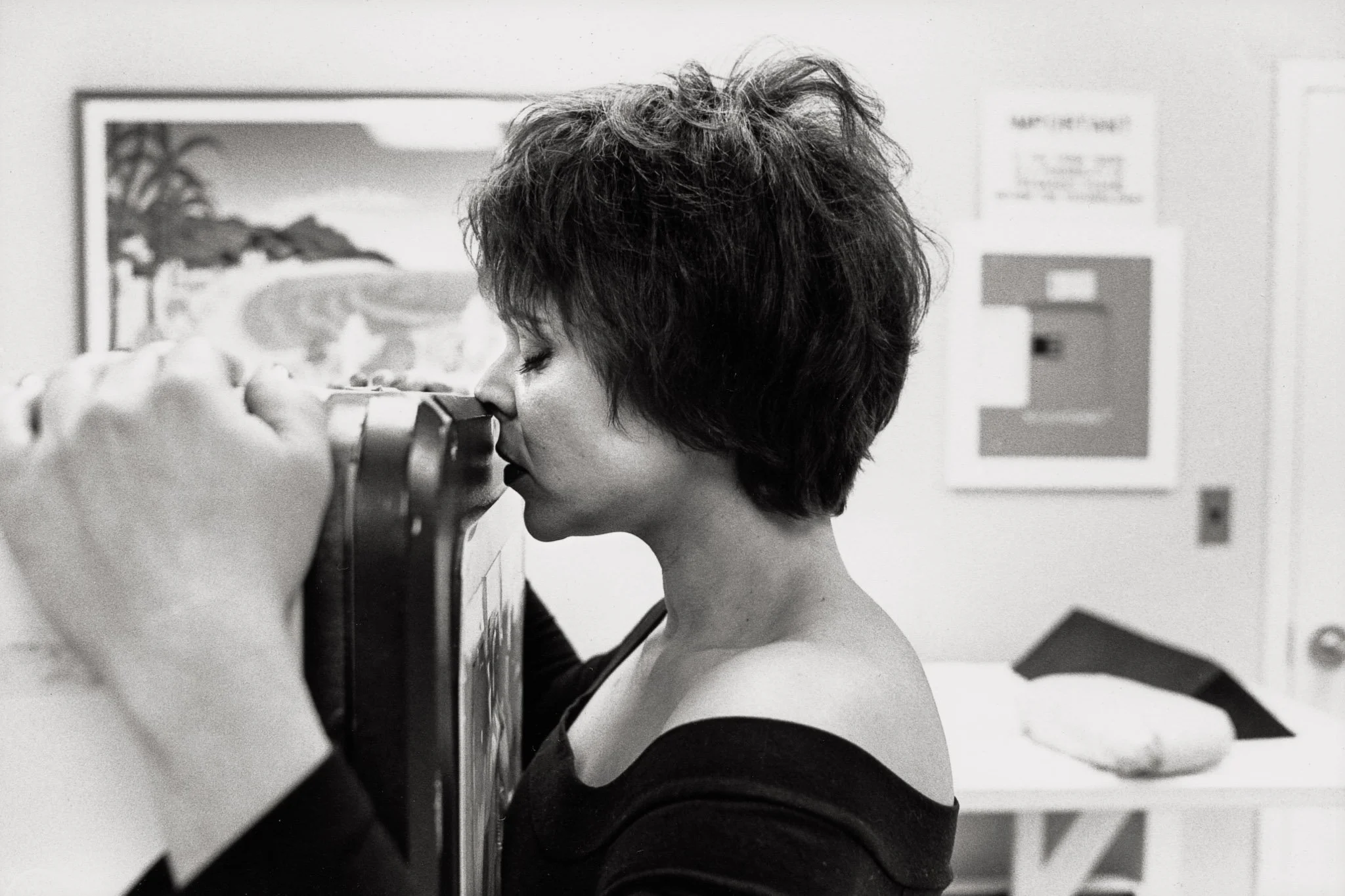 A woman in a doctor's office stands clutching a CT machine, pressing her chest against the sensor, her eyes closed in quiet concentration and prayer, hoping for negative results as the machine scans for the emergence of new cancer tumors.