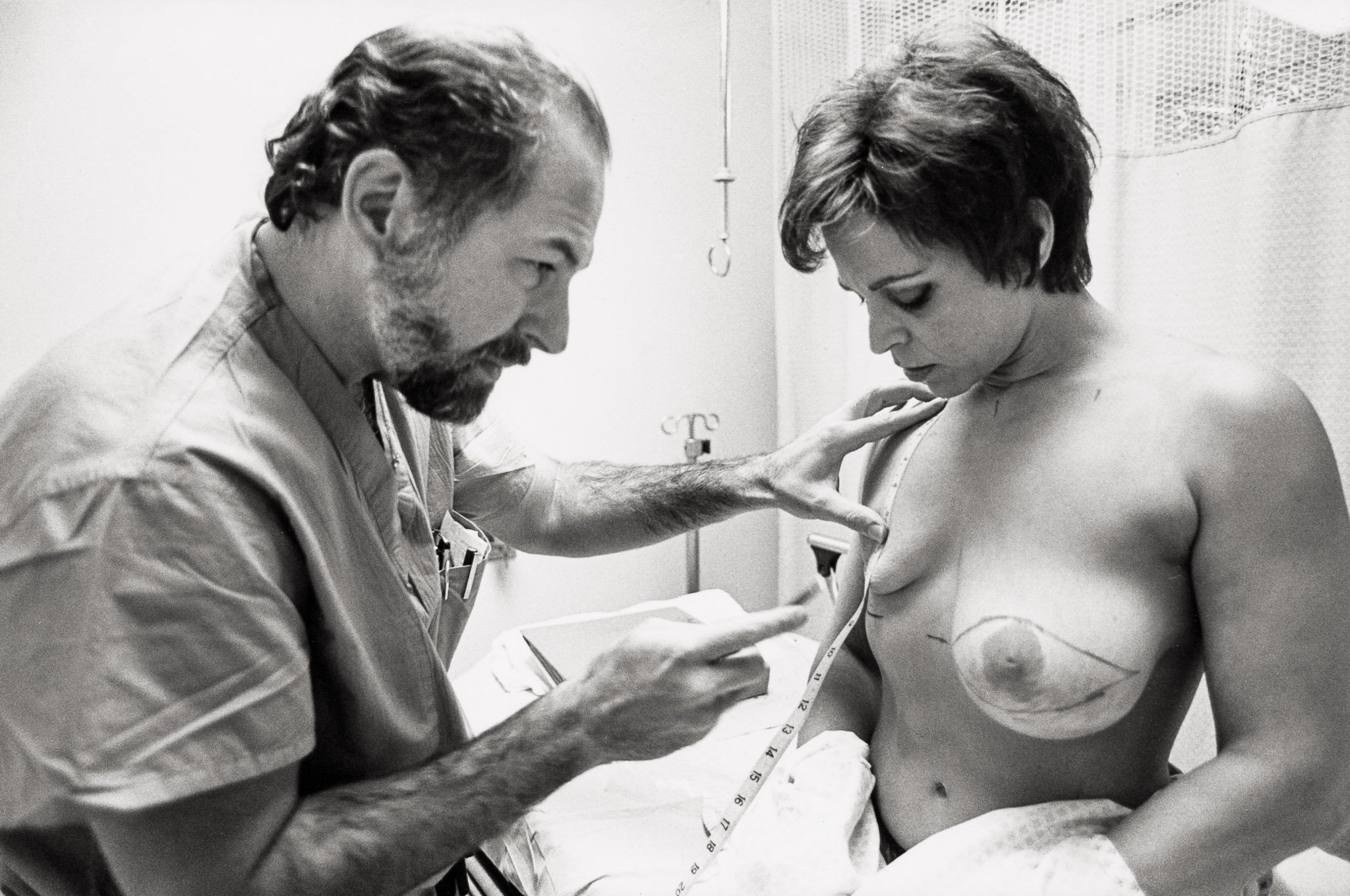 A plastic surgeon makes final measurements in a pre-operation ward prior to a woman's mastectomy, drawing incision lines on her chest.