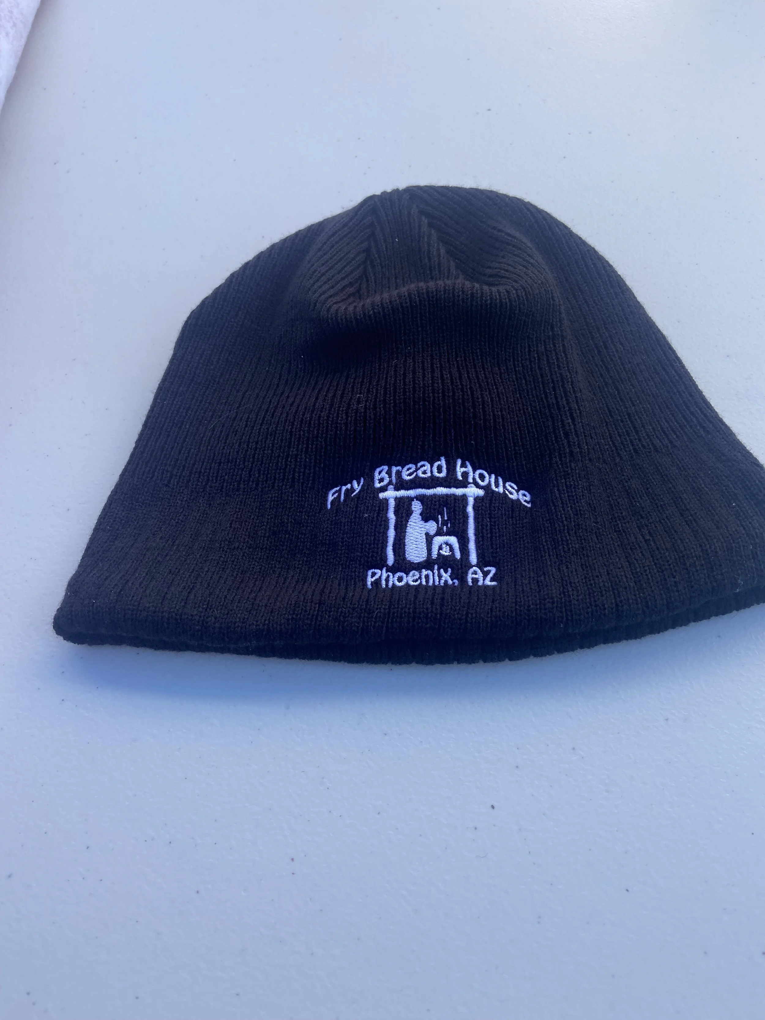 Black knit beanie hat with white embroidery reading "Fry Bread House, Phoenix, AZ," featuring a small graphic of a oven with a spatula.