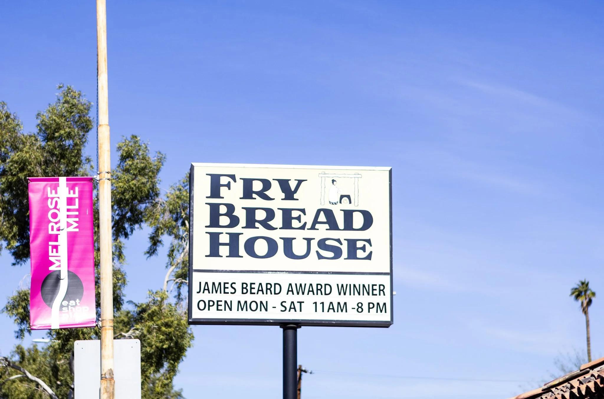 Sign for Fry Bread House with business hours from Monday to Saturday, 11 am to 8 pm, and an illustration of a person near an oven or fireplace.