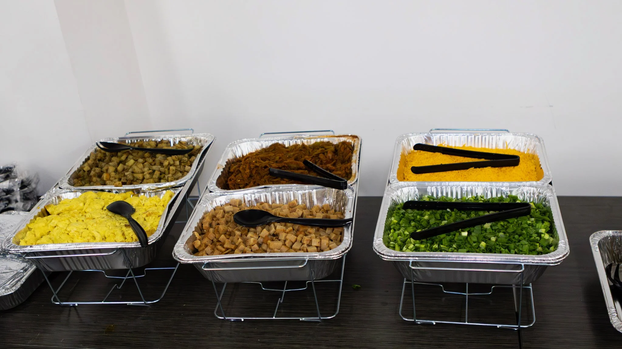 Buffet tray with scrambled eggs, diced chicken, shredded beef, diced pork, vegetable salad, pumpkin mash, and green salad on a dark table.