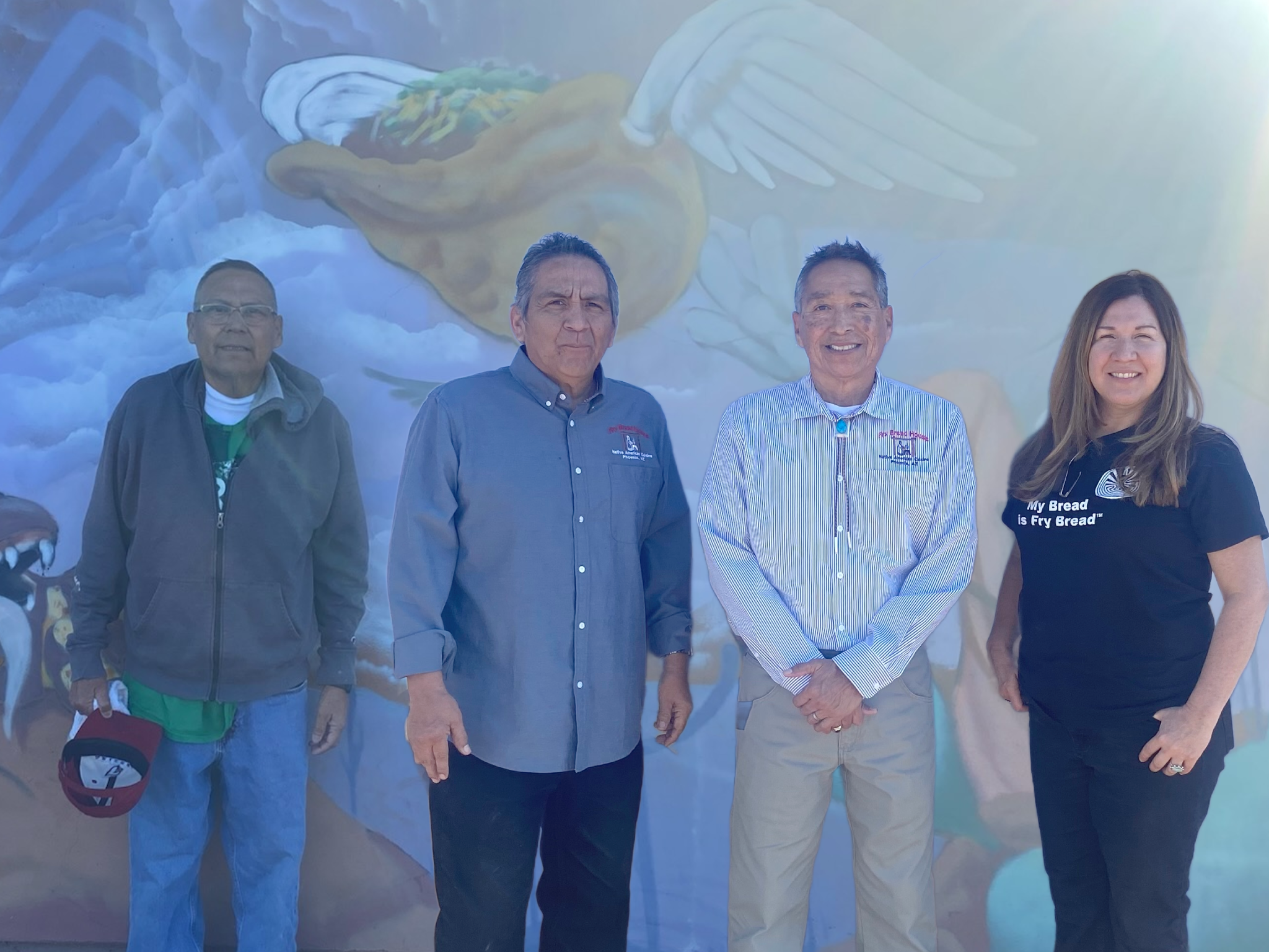 Four people standing in front of a mural depicting angel wings and a bread loaf with wings.