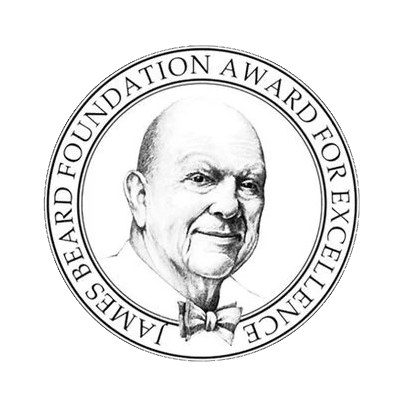 Black and white illustration of a bald man in a tuxedo with a bow tie, surrounded by a circular border reading 'James Beard Foundation Award for Excellence'.