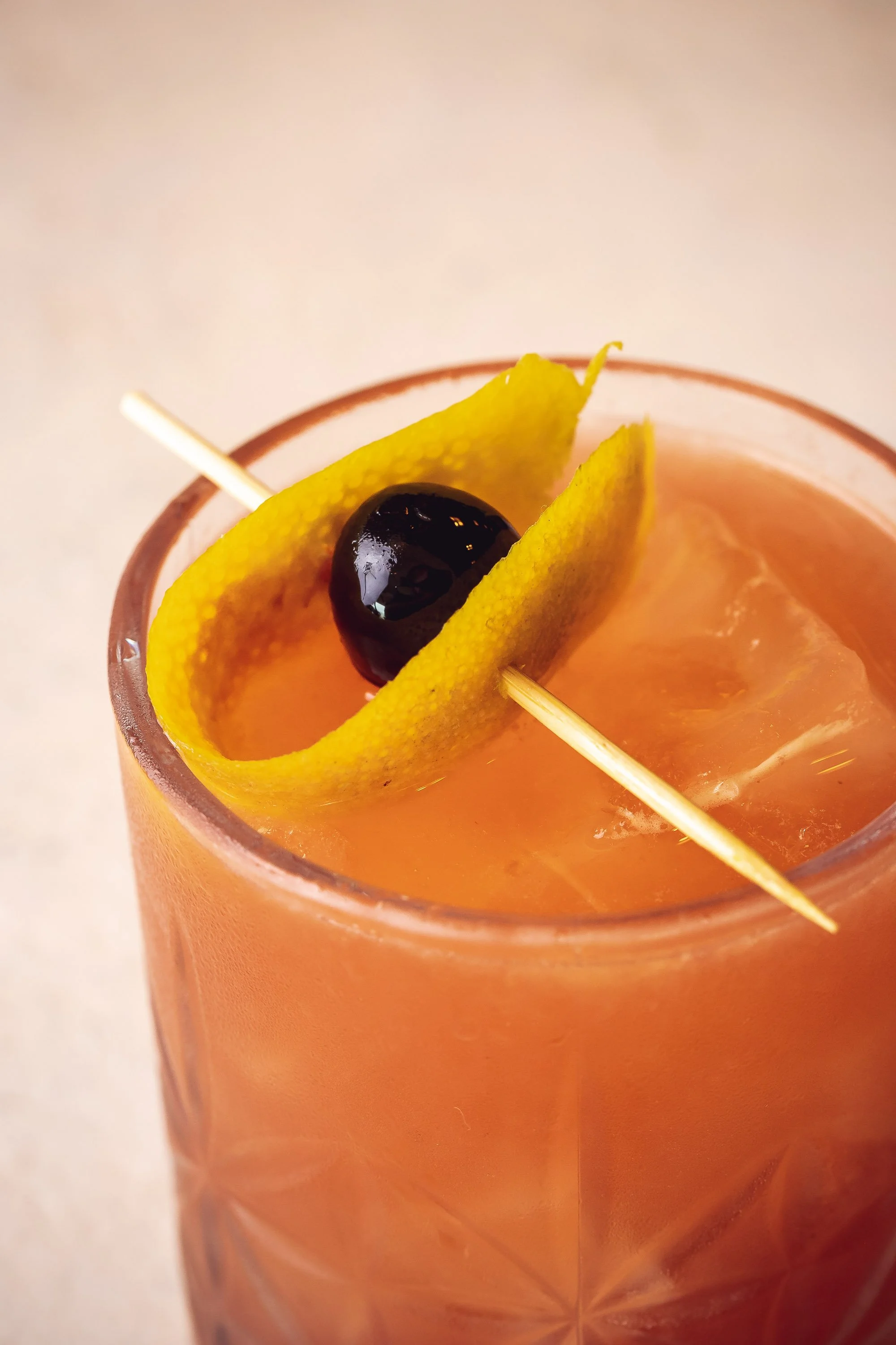 Close-up of amber cocktail over ice with orange peel and cherry garnish in faceted rocks glass
