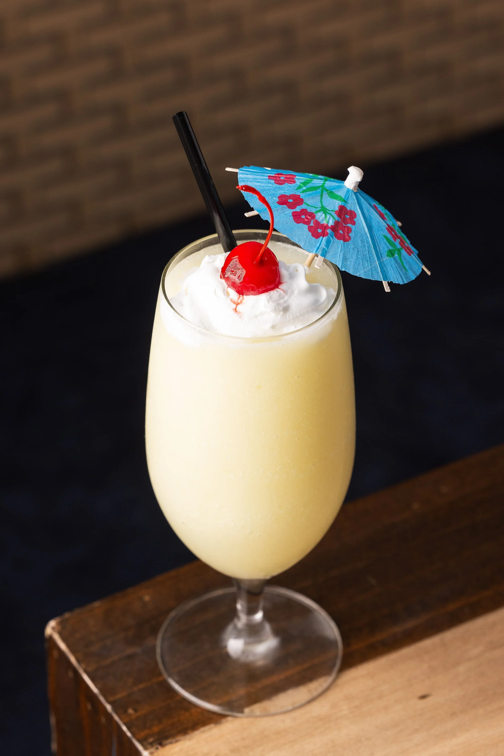 Frozen tropical cocktail topped with whipped cream, cherry, and blue paper umbrella in tall stemmed glass