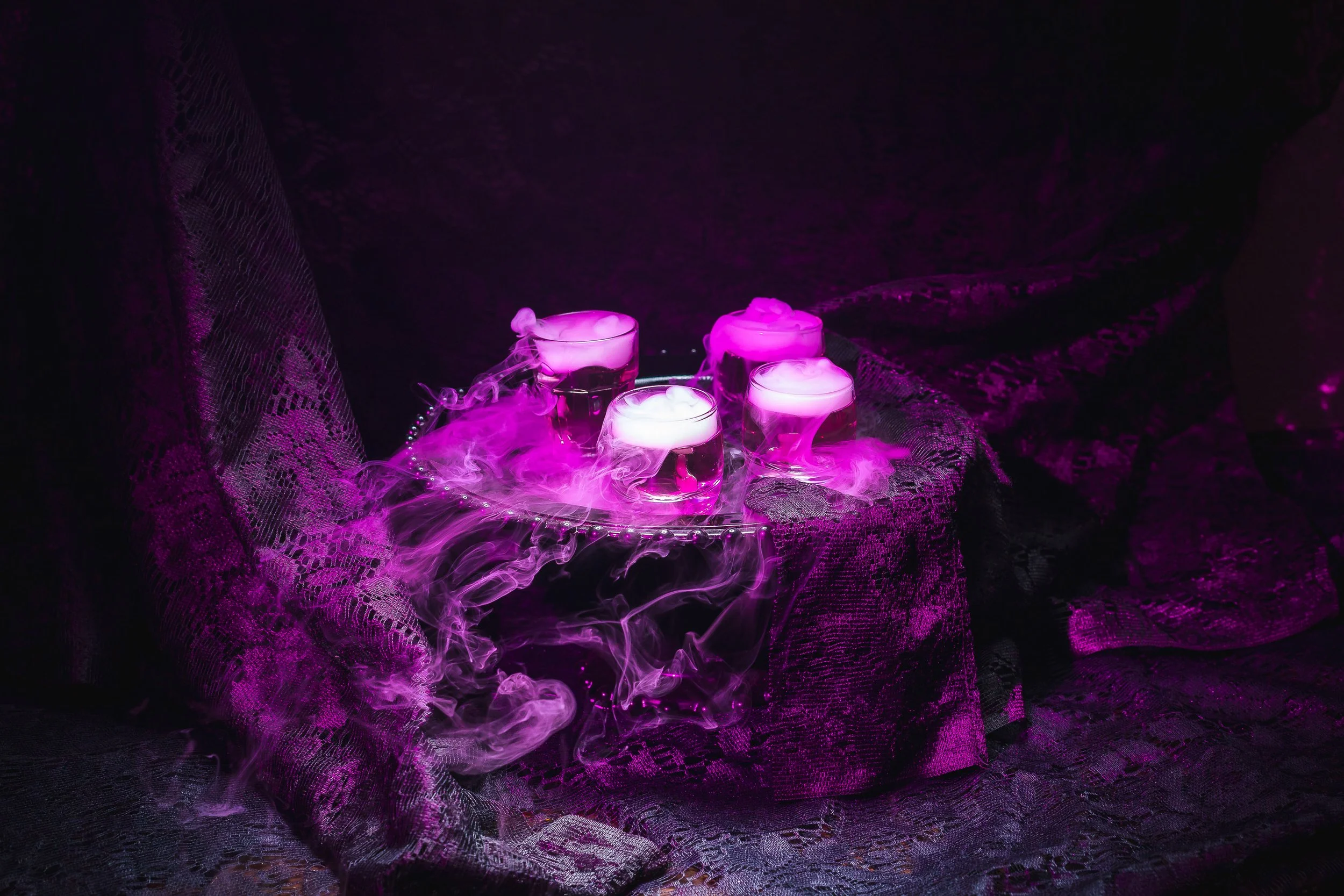Moody smoked cocktail flight with theatrical vapor, dramatic purple lighting, and dark styled bar scene
